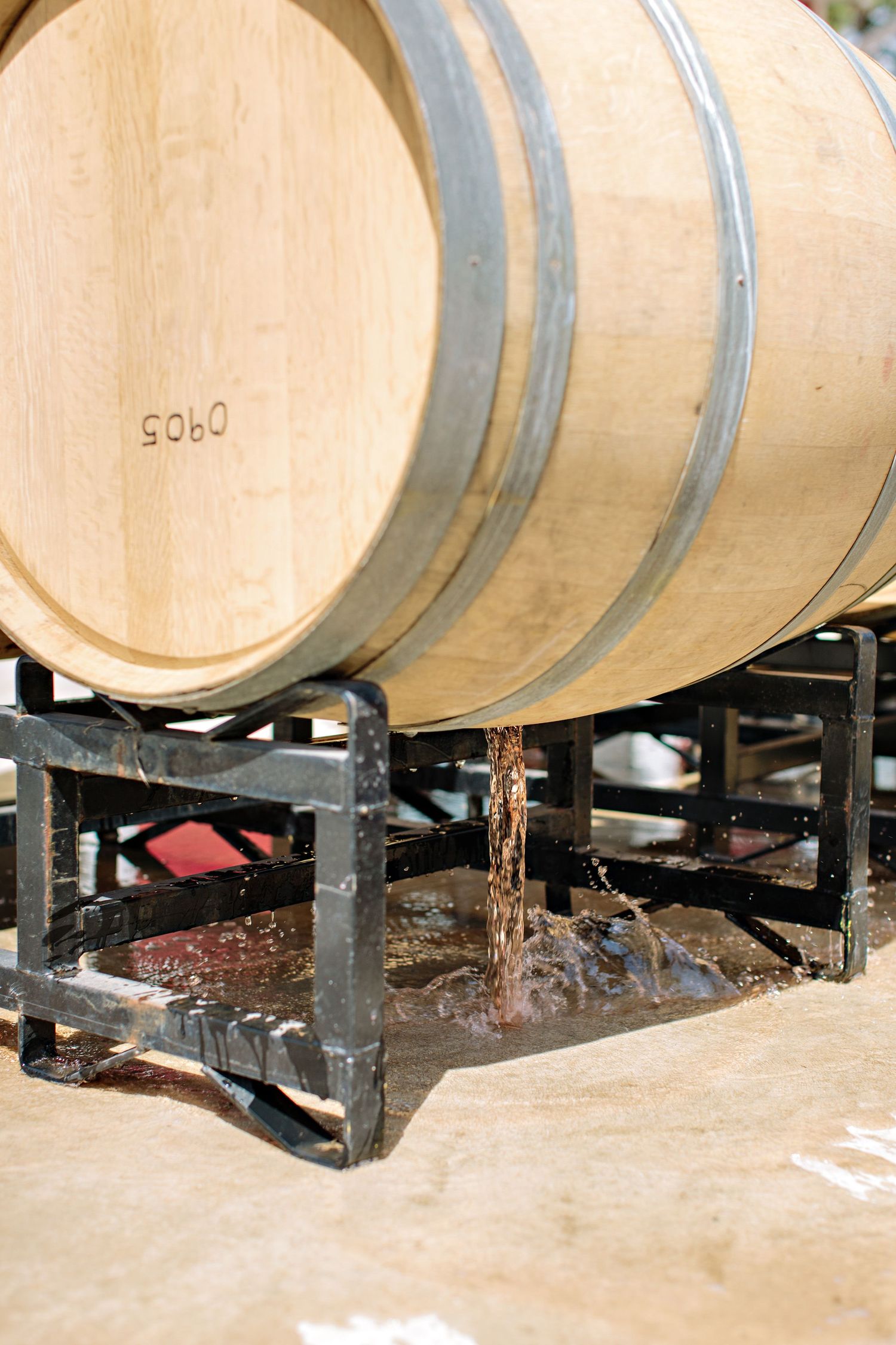 Liquid dripping from a wooden wine barrel mounted on black metal racks during the winemaking process.