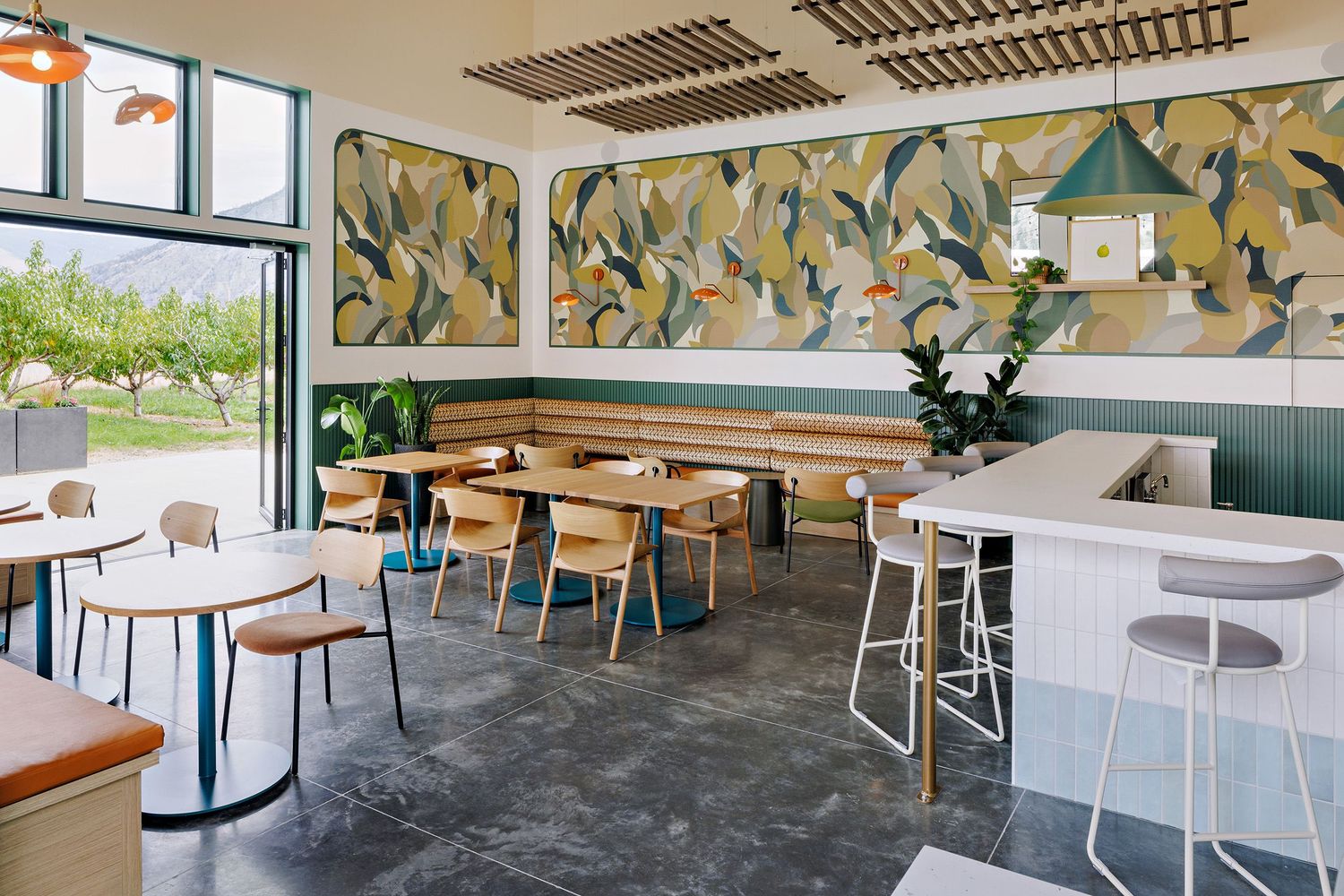 Modern cafe interior with colorful botanical wallpaper, wooden tables, and white chairs on concrete flooring.