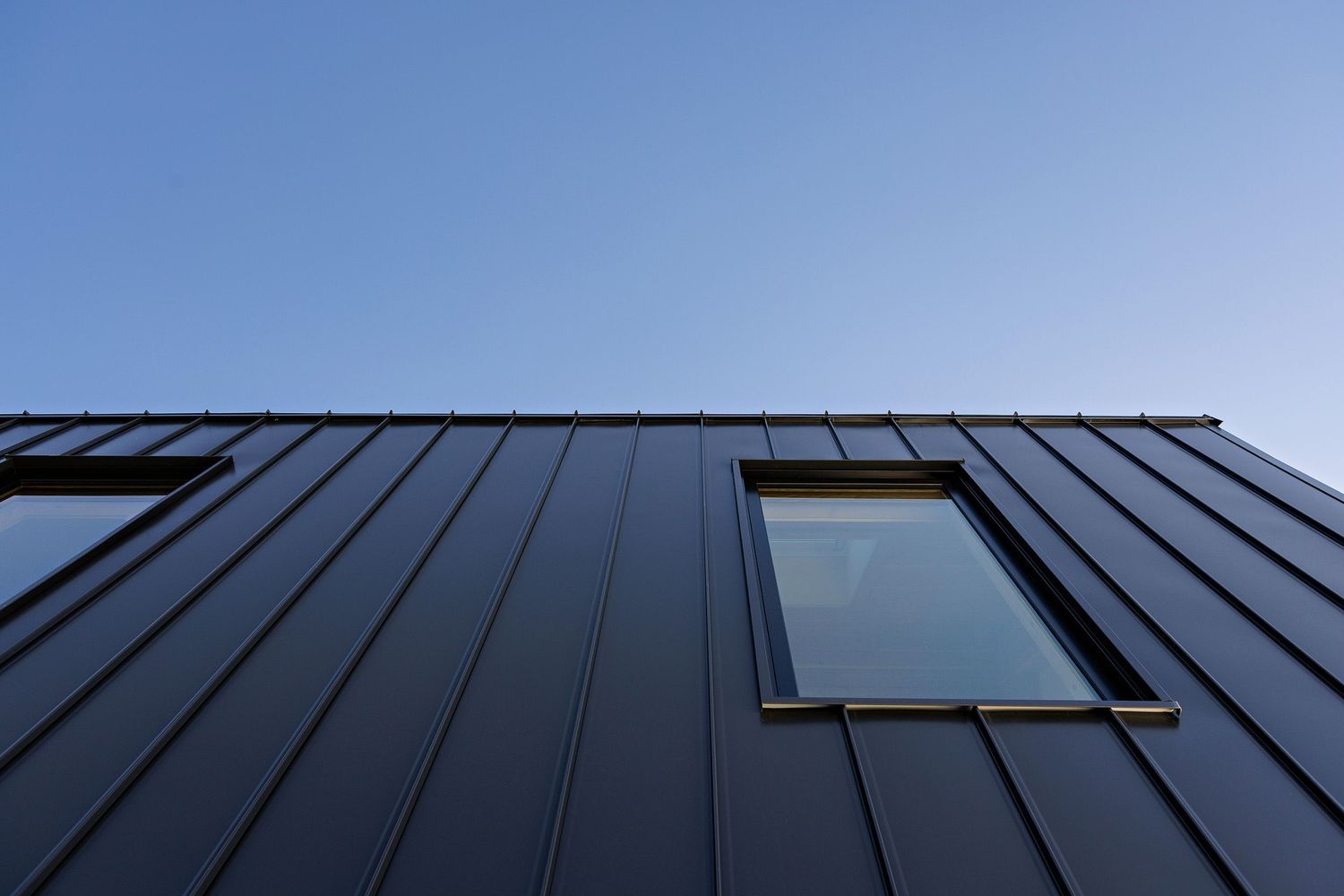 Modern black metal exterior wall with a minimalist skylight window against blue sky.