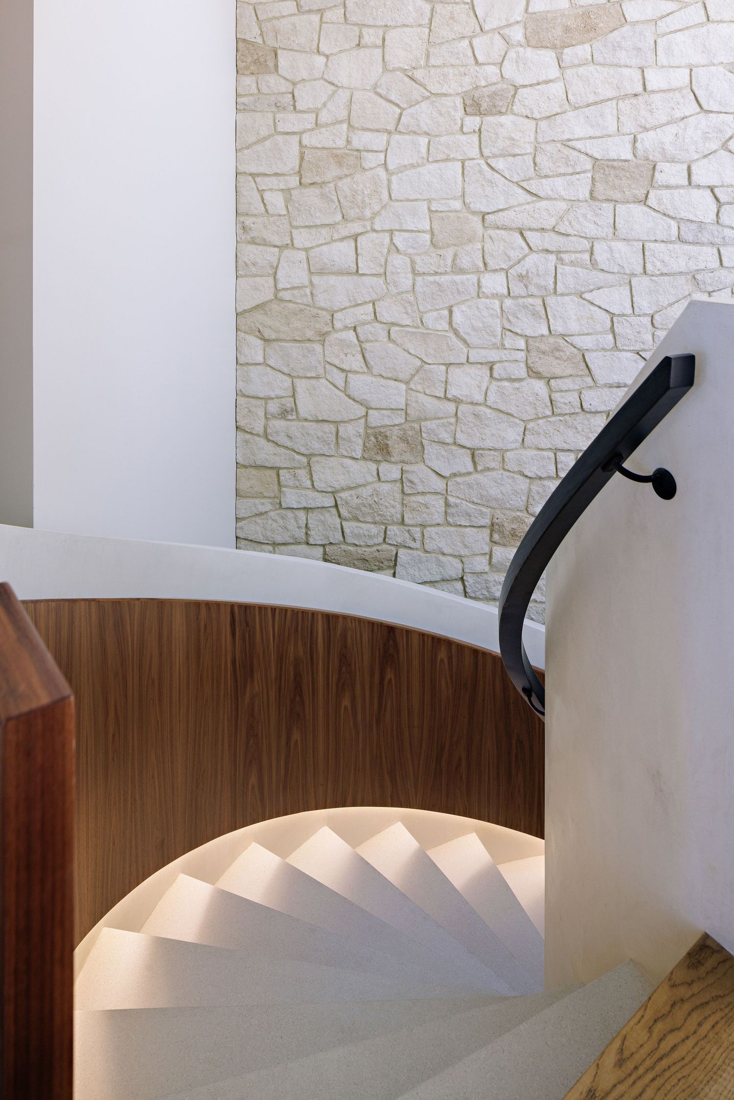Modern spiral staircase with white steps and wooden curved wall against textured stone background.
