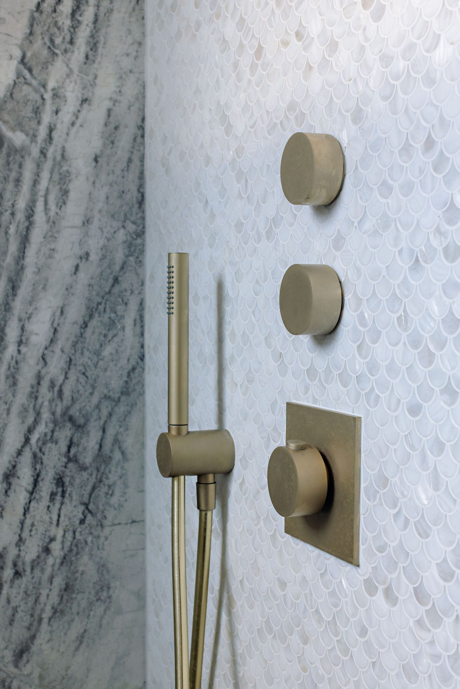 Modern brushed gold bathroom fixtures mounted on white marble tile wall with hexagonal pattern detail.