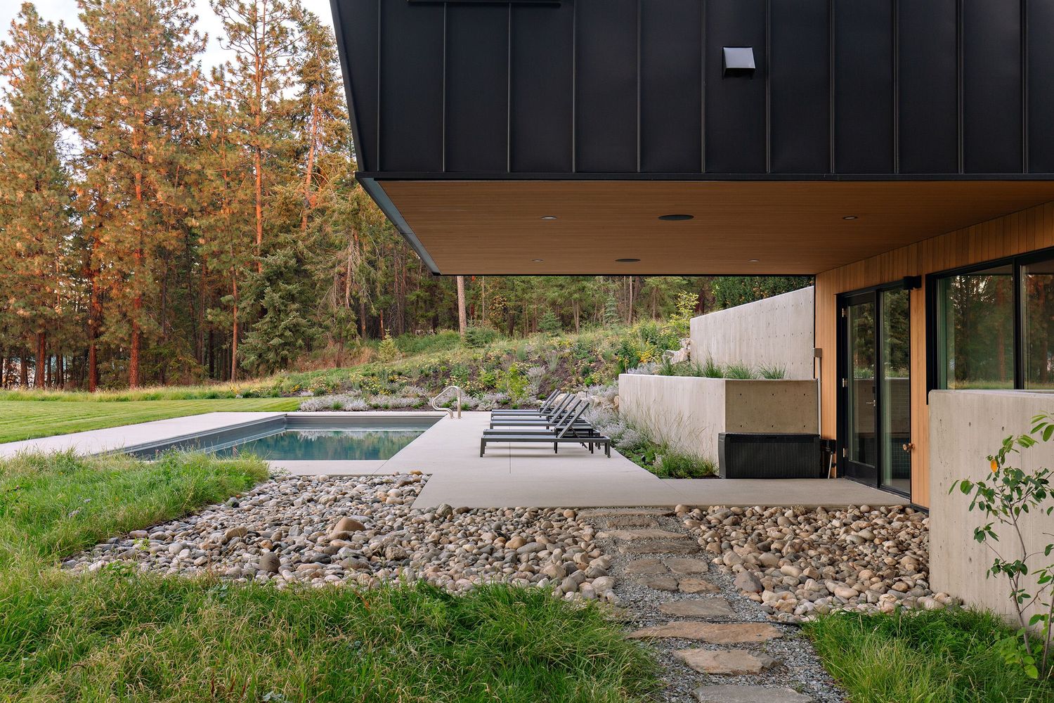 Modern home exterior with stone pathway and landscaping features black upper level and concrete lower level design.