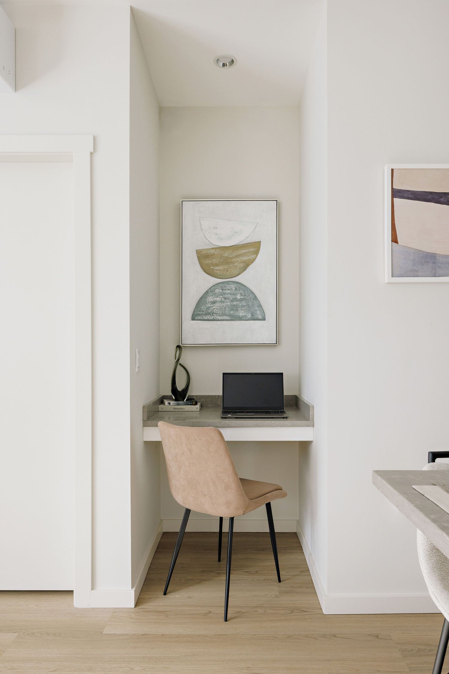 Minimalist home office nook with pink velvet chair, built-in white desk, and modern abstract art on the wall.