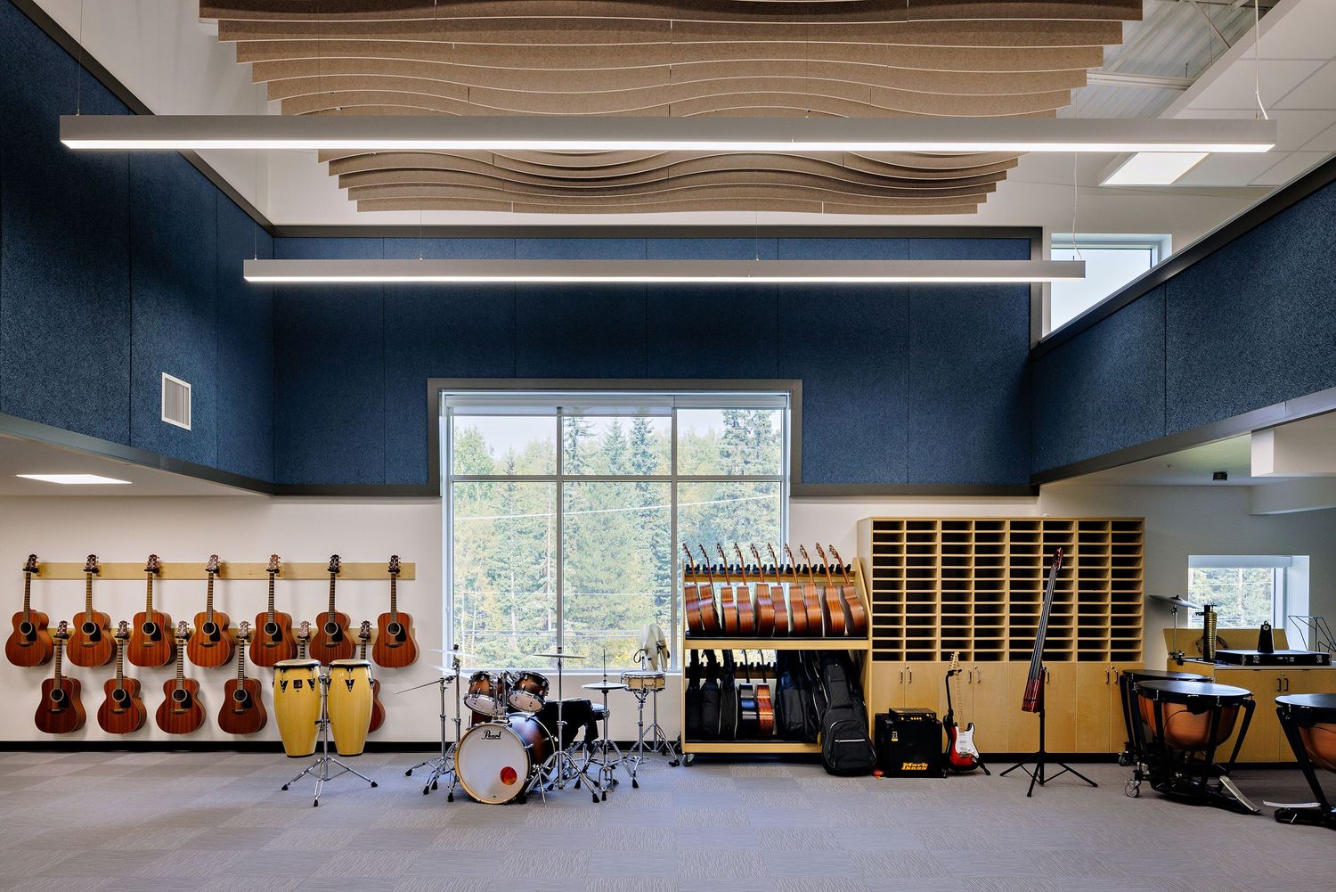 Music practice room with blue walls featuring mounted violins, drum set, music stands and wooden storage cubbies with window.
