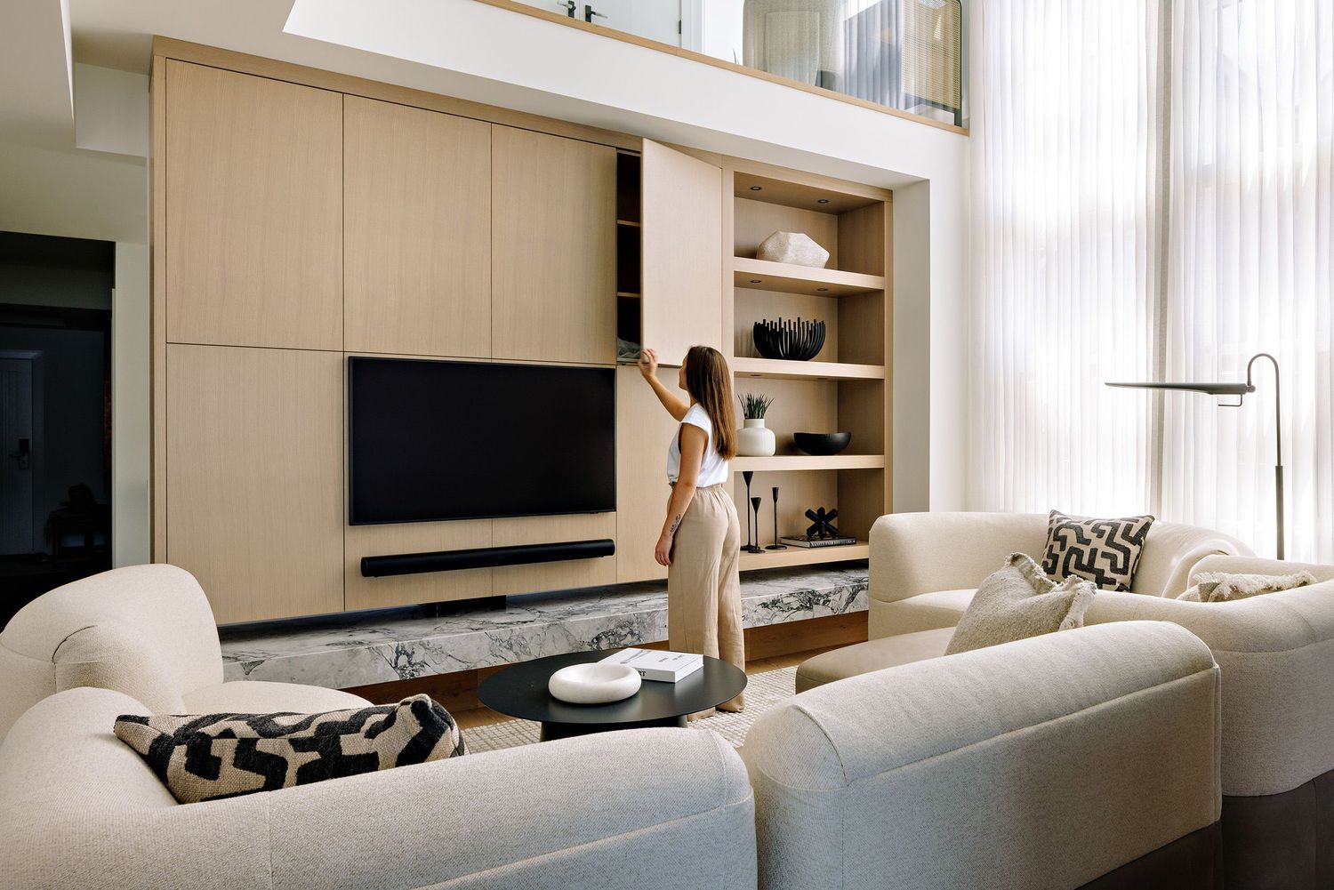 Modern living room with beige built-in entertainment wall, white sectional sofa and tall windows with natural light.