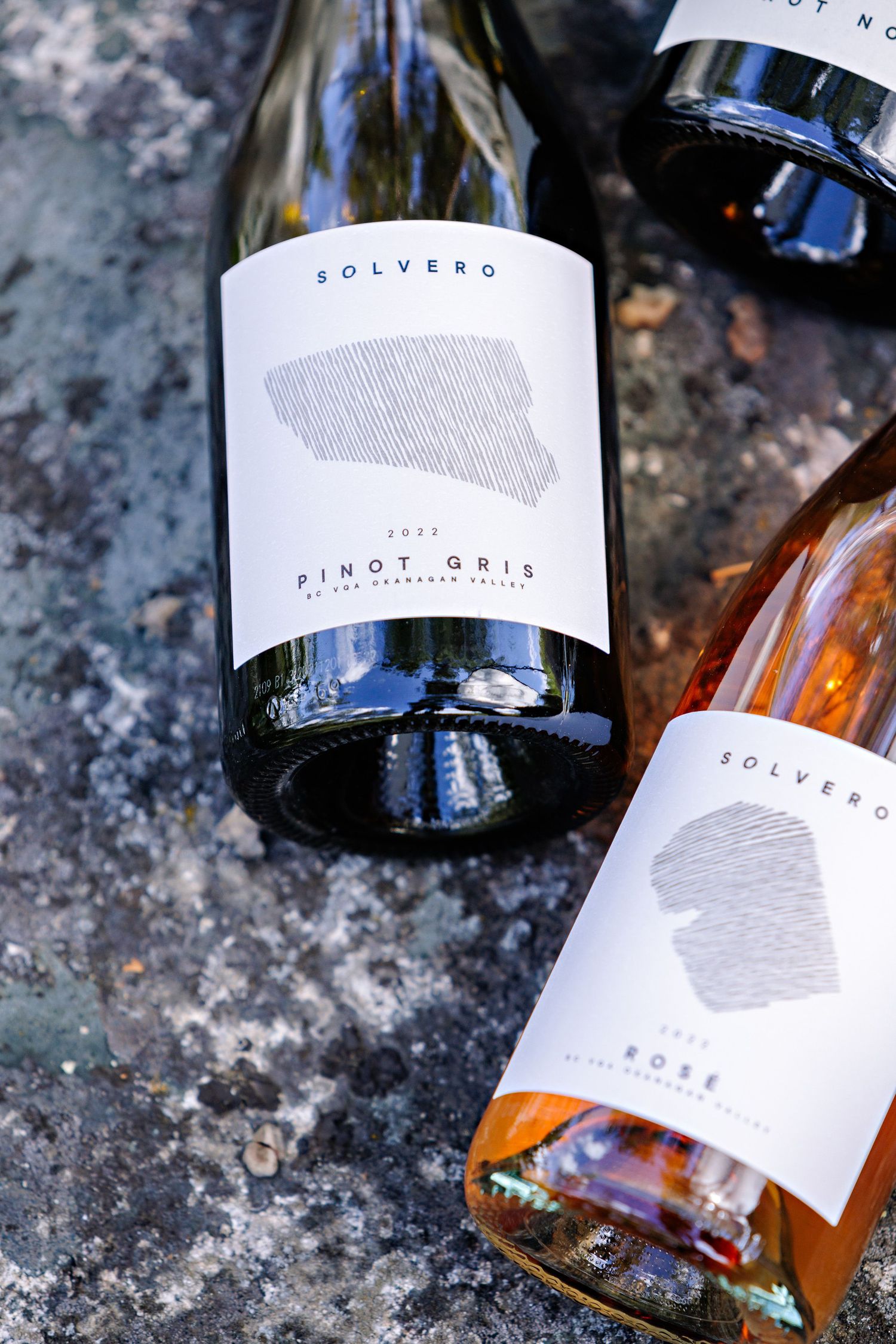 Three bottles of Solvero wine with minimalist grey labels displayed on stone surface.