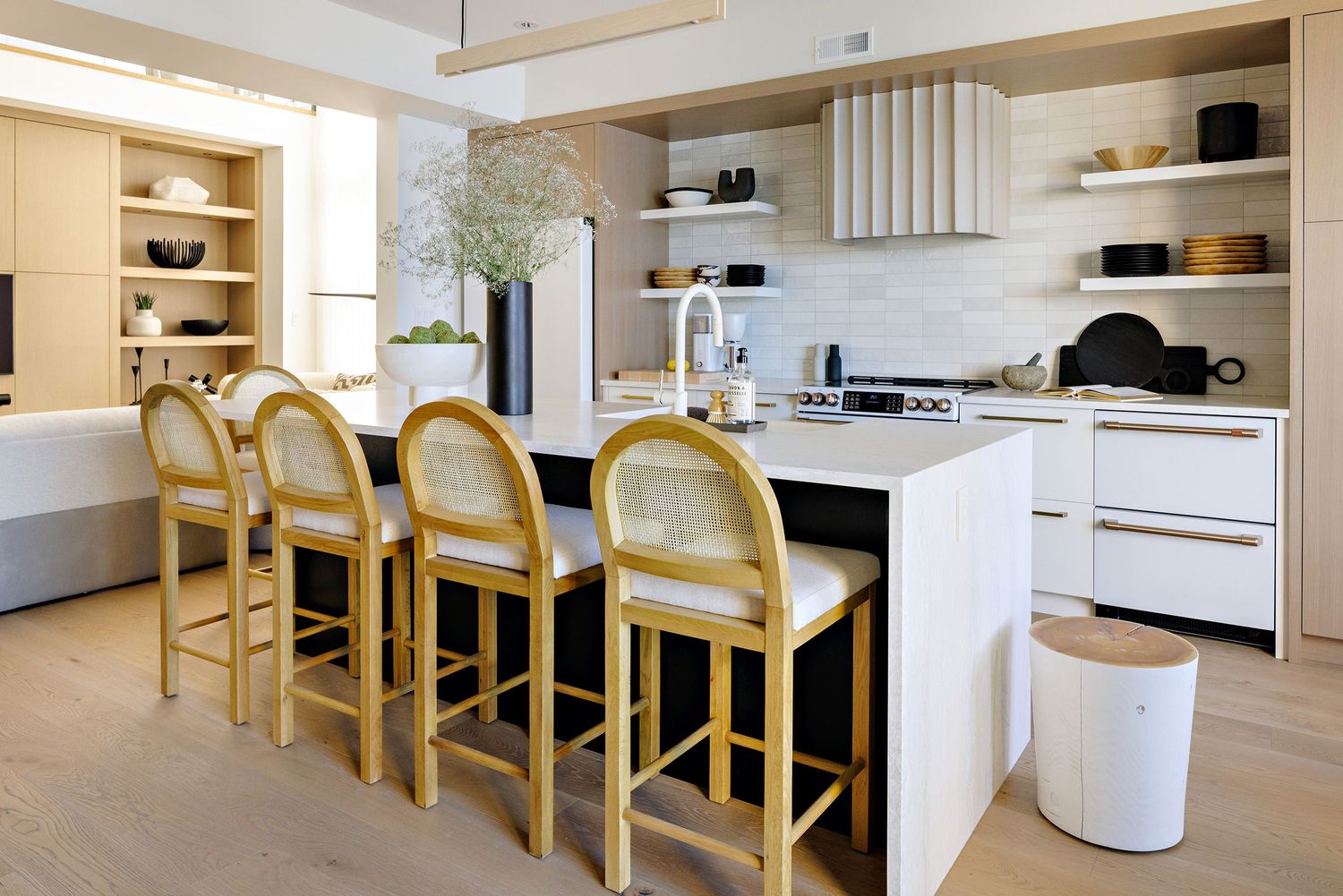 Bright kitchen with wooden bar stools and white island featuring open shelving.