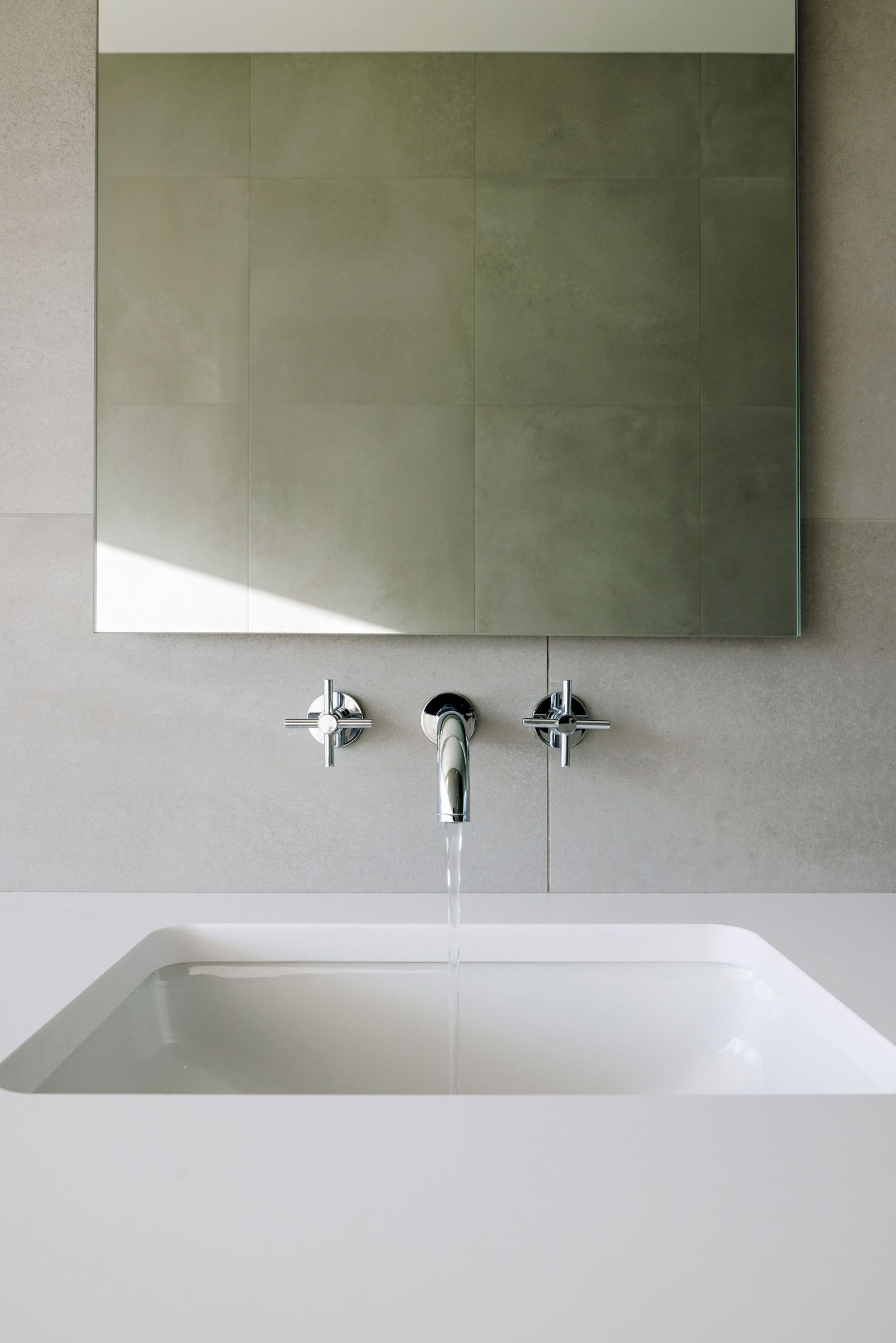 Modern minimalist bathroom featuring a rectangular white sink basin with wall-mounted chrome faucets and large mirror above.