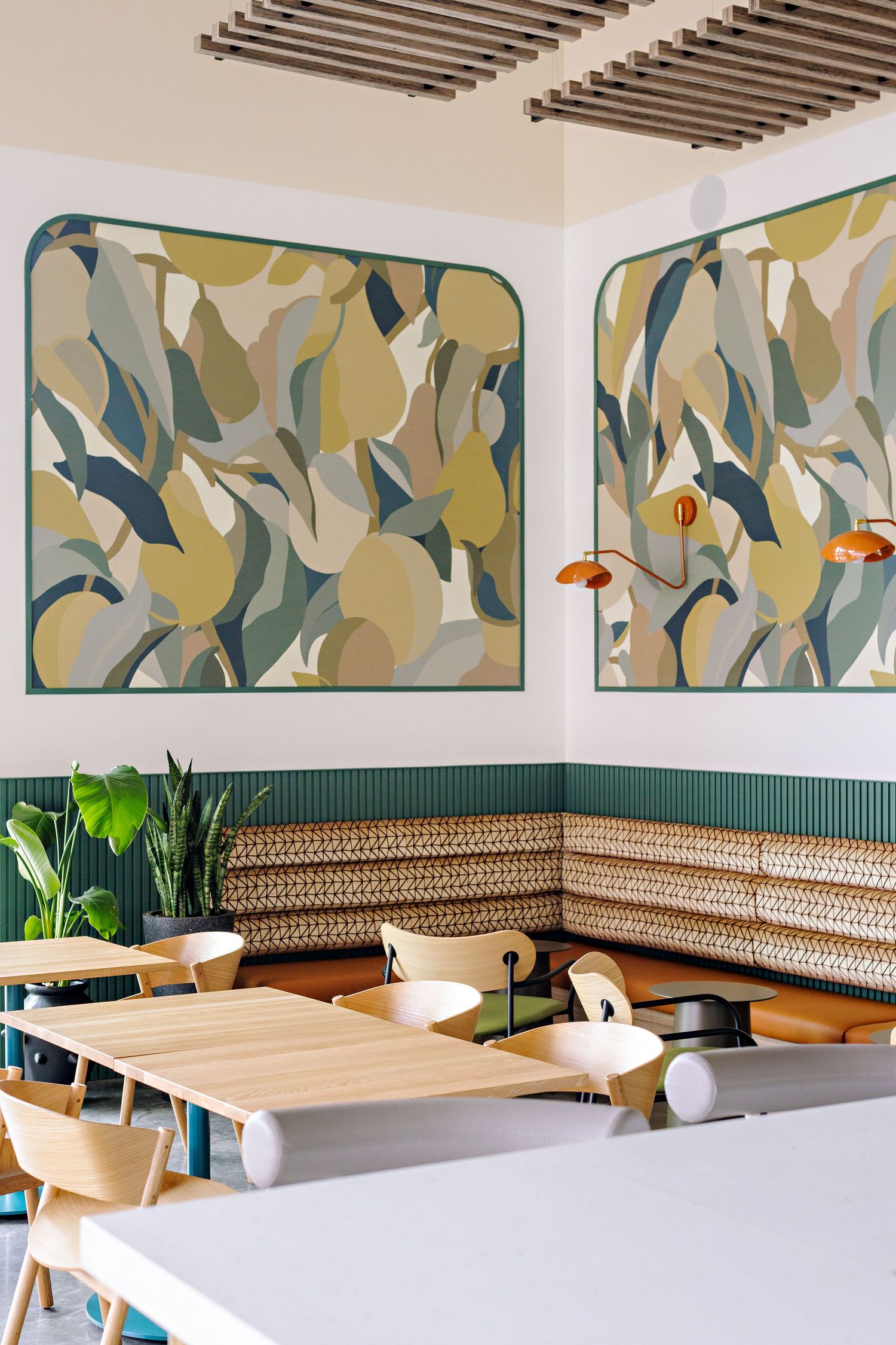 Modern restaurant interior with abstract wall art, wooden bench seating, and hanging orange pendant lamps.