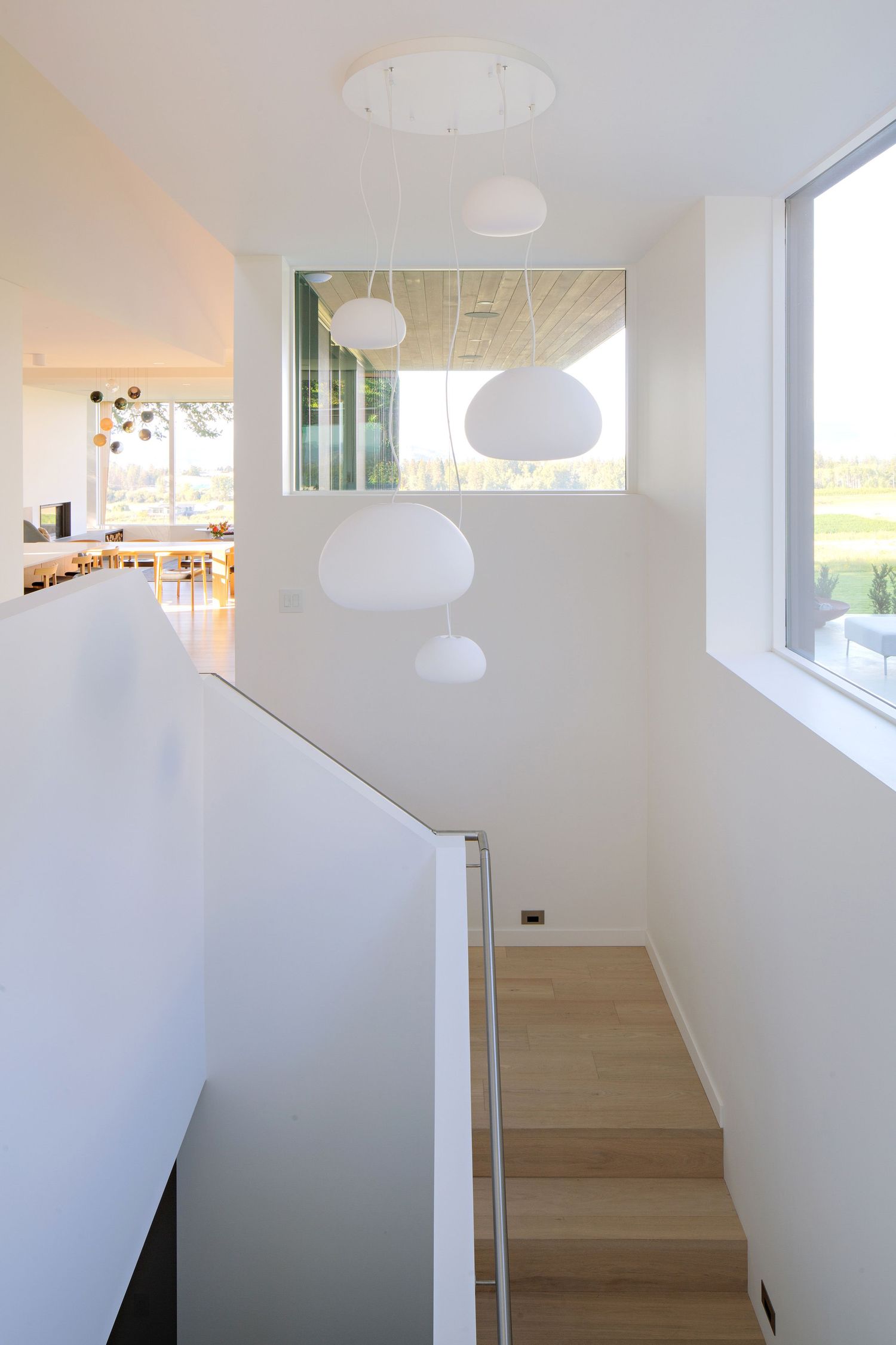 Modern white stairwell with round pendant lights and natural light flowing through a window shows minimalist interior design.