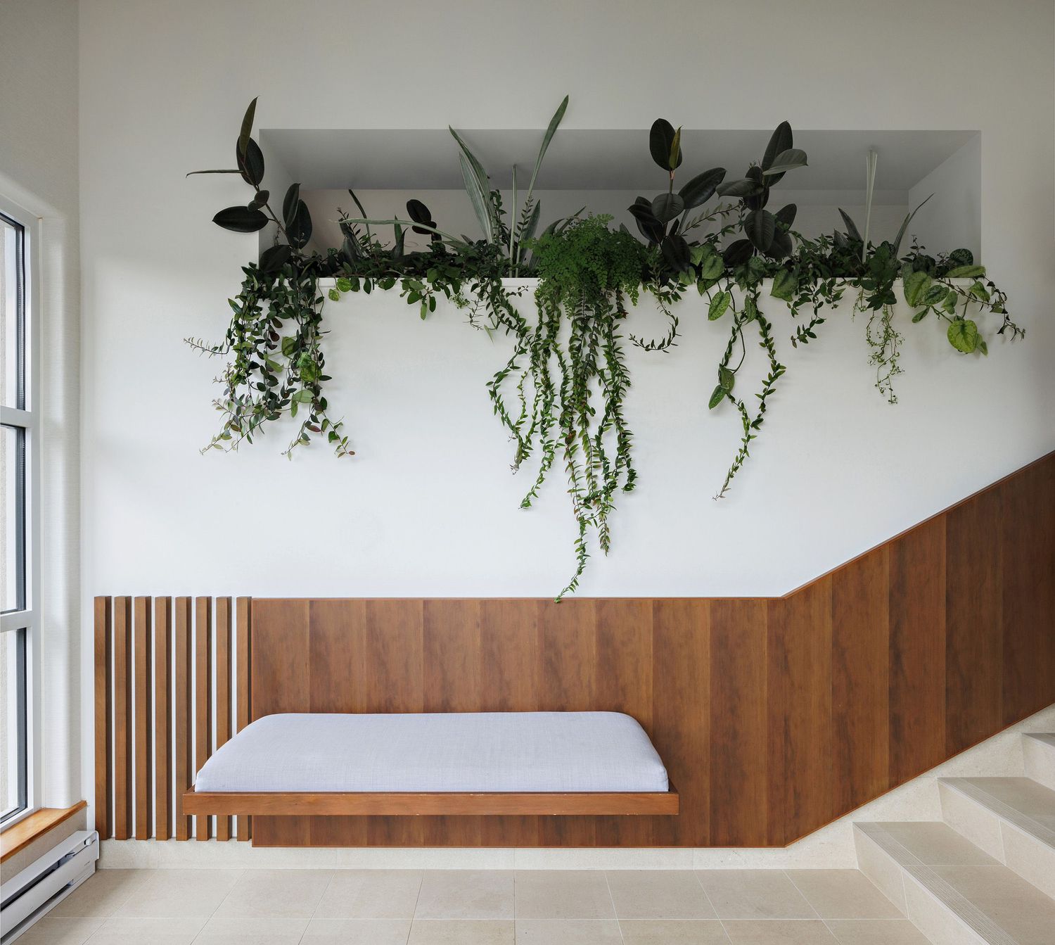 Modern interior design featuring a wooden bench seat with hanging plants and greenery suspended from the ceiling.