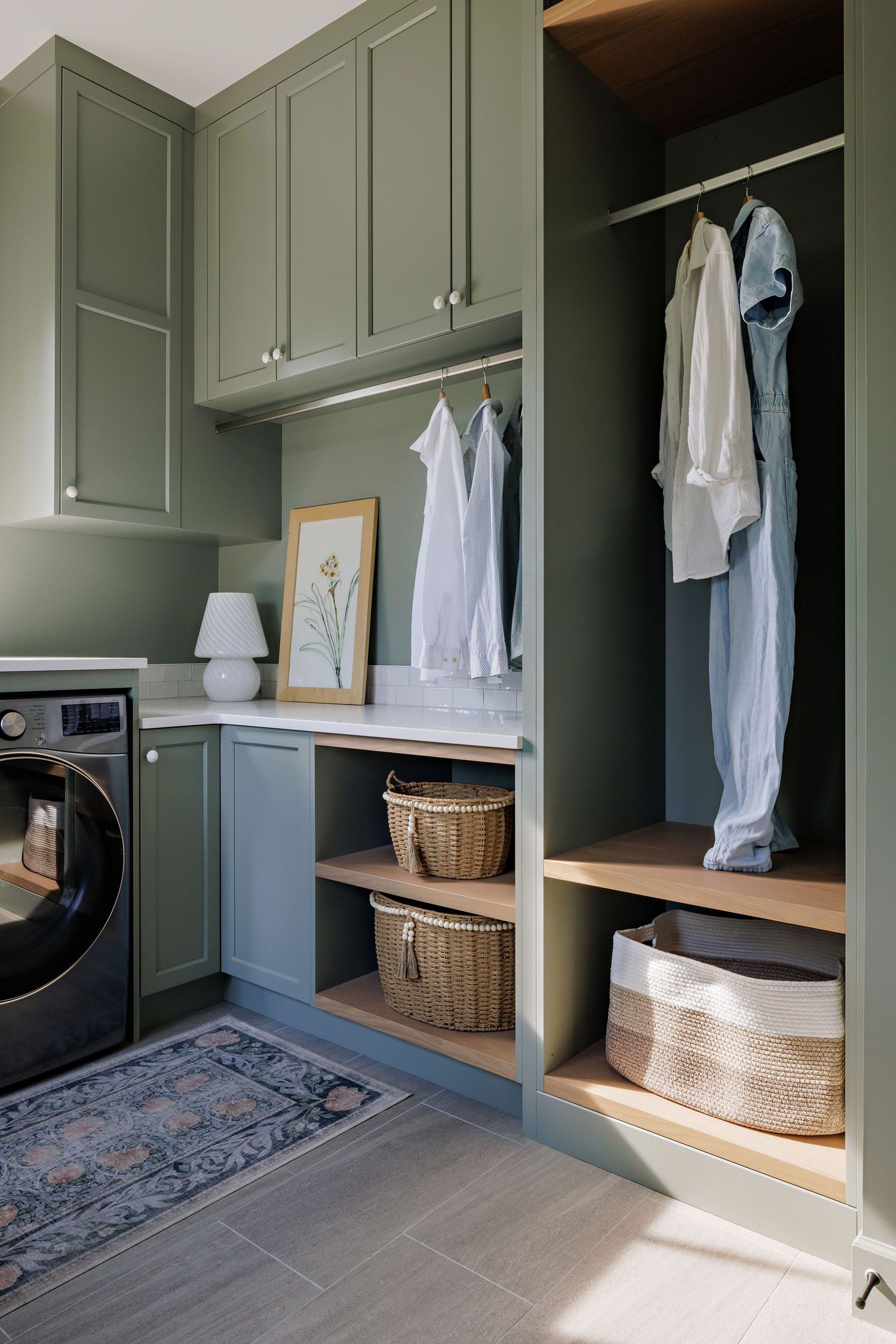 Stylish mudroom featuring sage green built-ins, dark wood bench, woven baskets, and a decorative blue patterned rug.