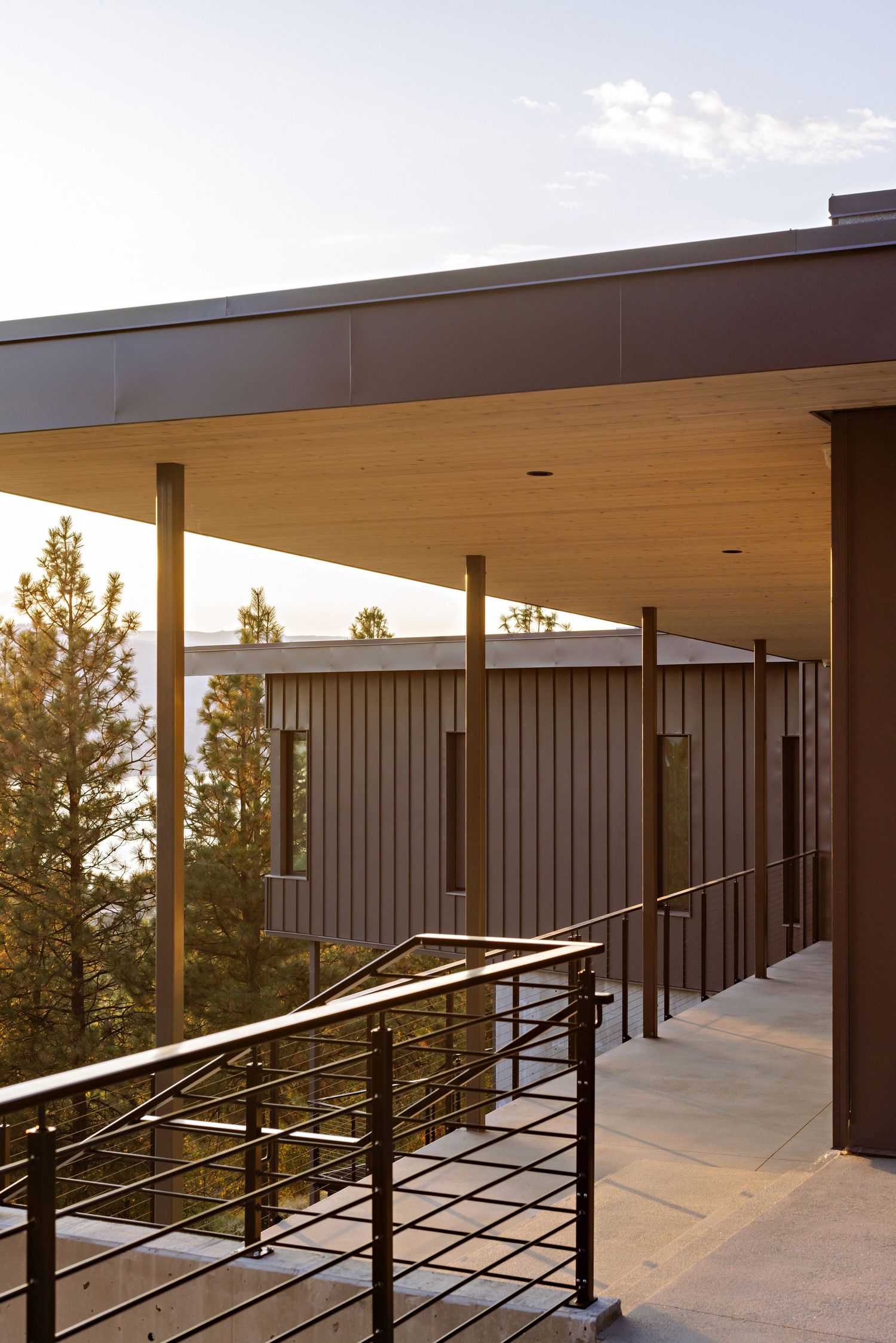 Modern architectural balcony with metal railings and wooden overhang showcasing mountain views at sunset.