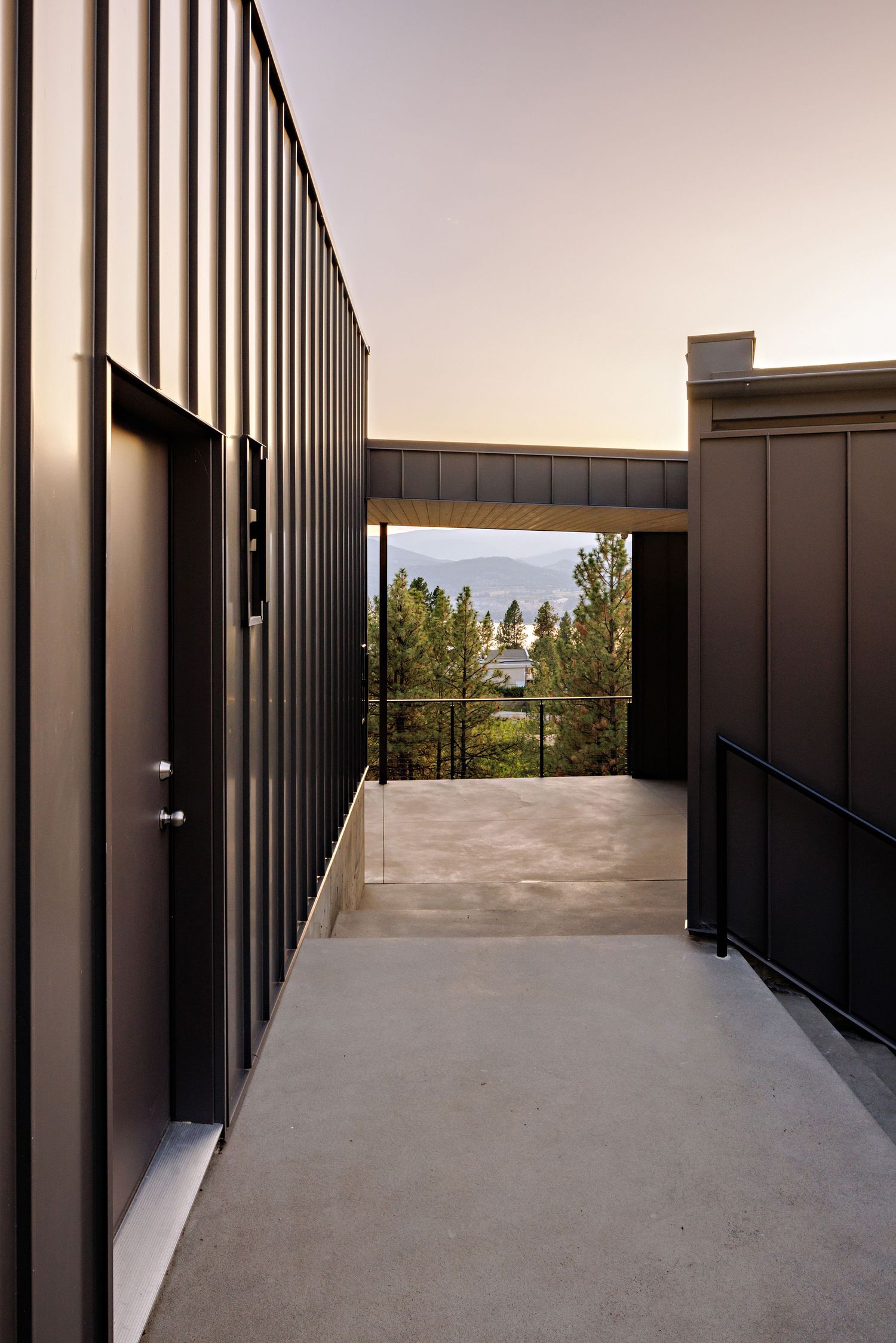 Modern building hallway with vertical metal panels framing a scenic mountain view through glass windows at sunset.