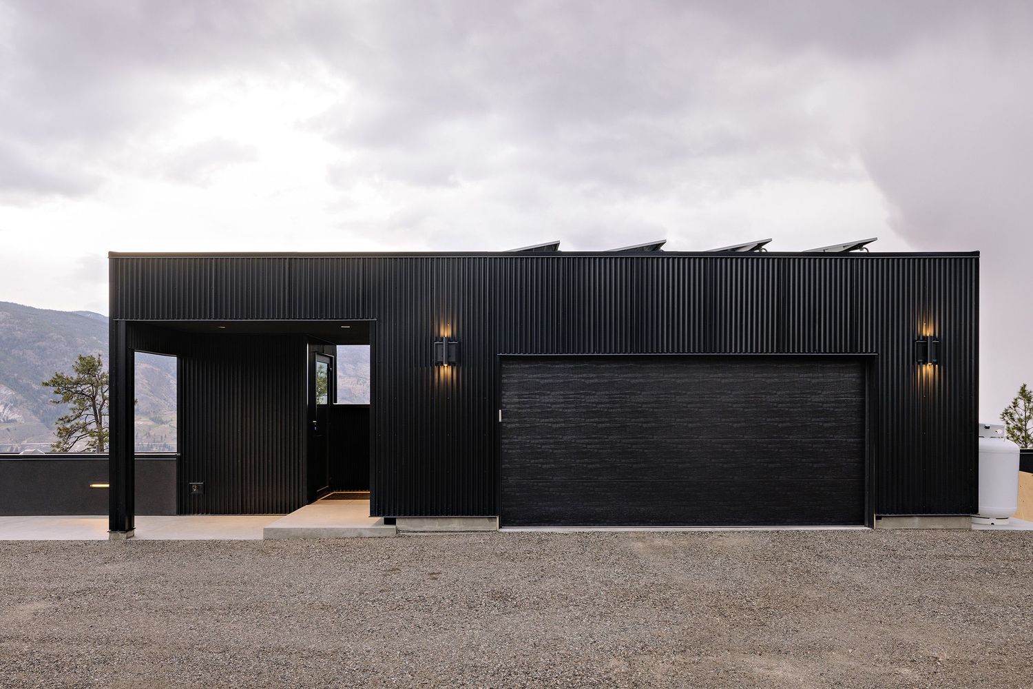 Modern black minimalist house with clean lines and wall-mounted sconces sits against a mountainous backdrop.