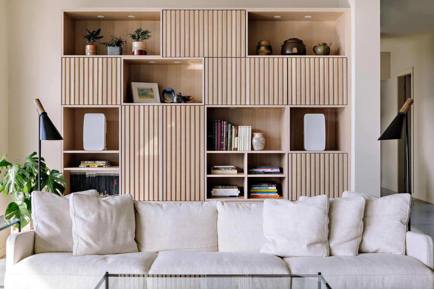 Modern living room with white sofa and built-in wooden storage unit featuring vertical slat sliding doors and open shelving.