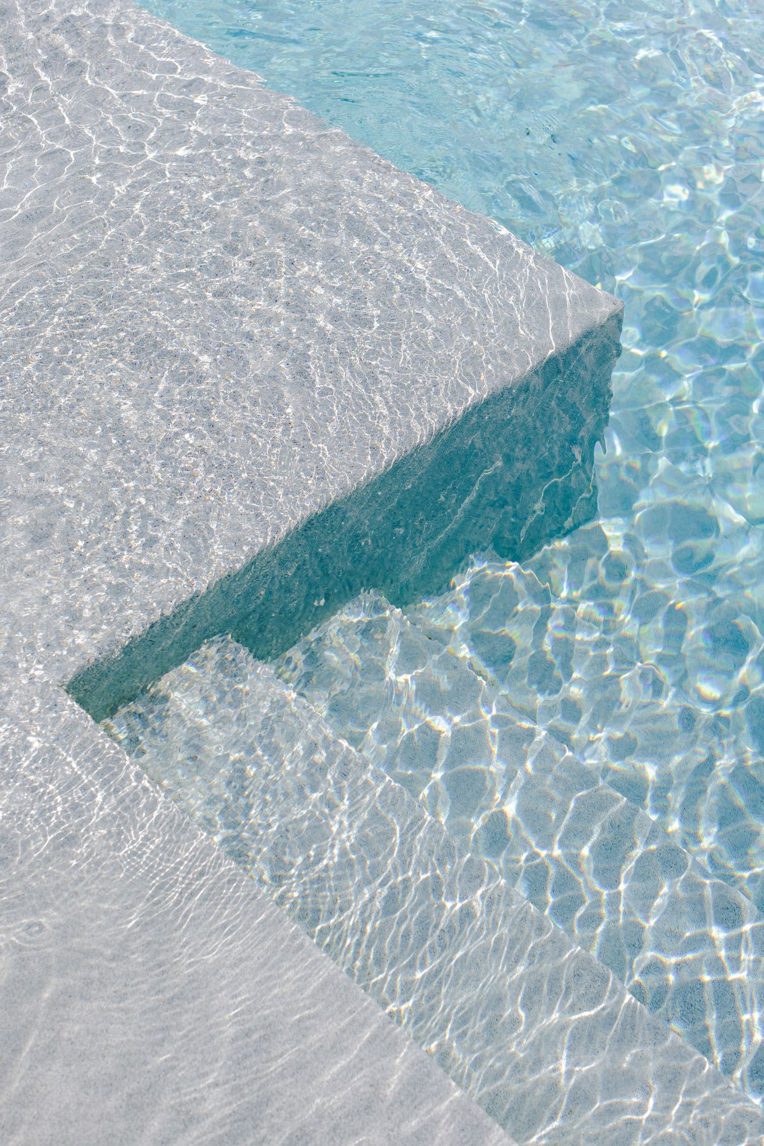 Sunlight creates rippling patterns on turquoise pool water against geometric concrete steps or ledge.