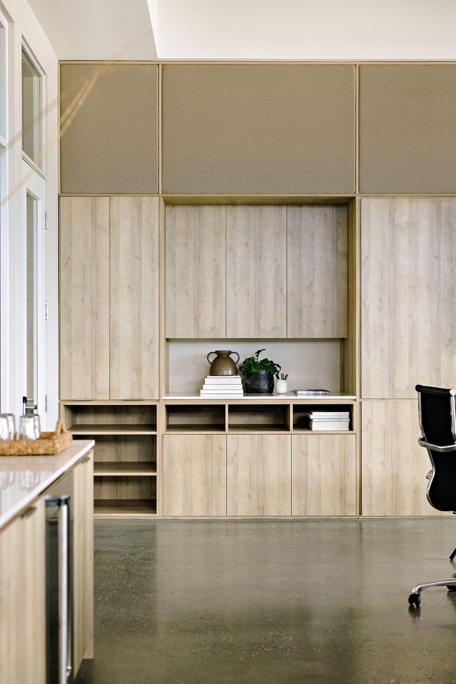 Modern office interior with built-in wooden storage unit, concrete floor and minimalist styling on display shelves.