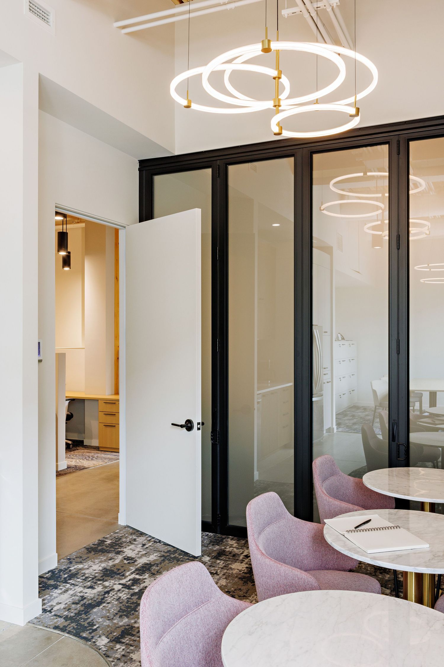 Modern office interior with circular LED pendant lights, pink velvet chairs, and glass partition doors.