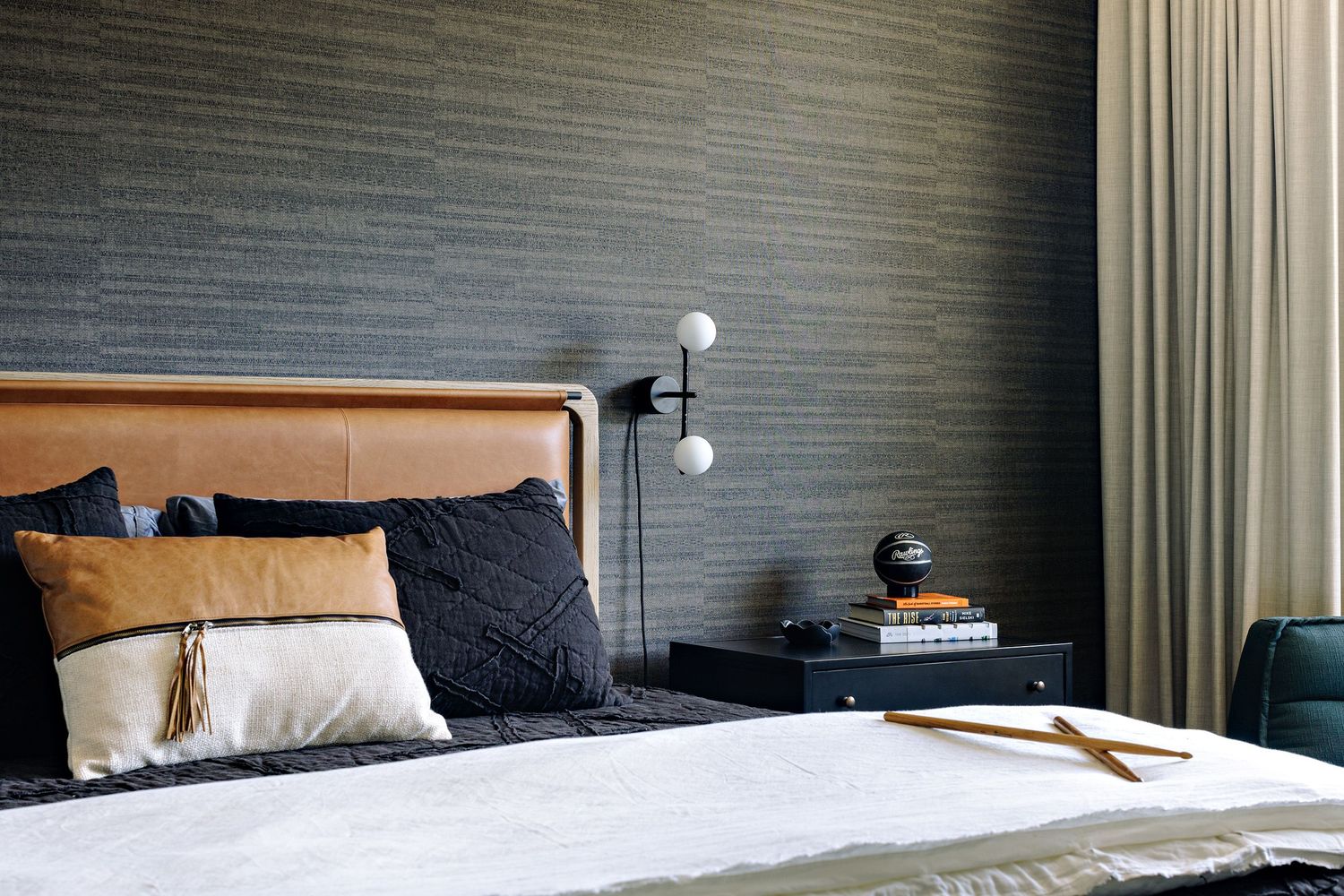 Modern bedroom with leather headboard, textured wallpaper, and contemporary lighting fixtures.