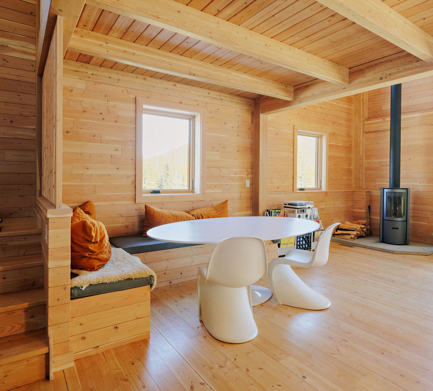 Modern Scandinavian dining space with wood-paneled walls, white tulip table and chairs, and black wood burning stove.
