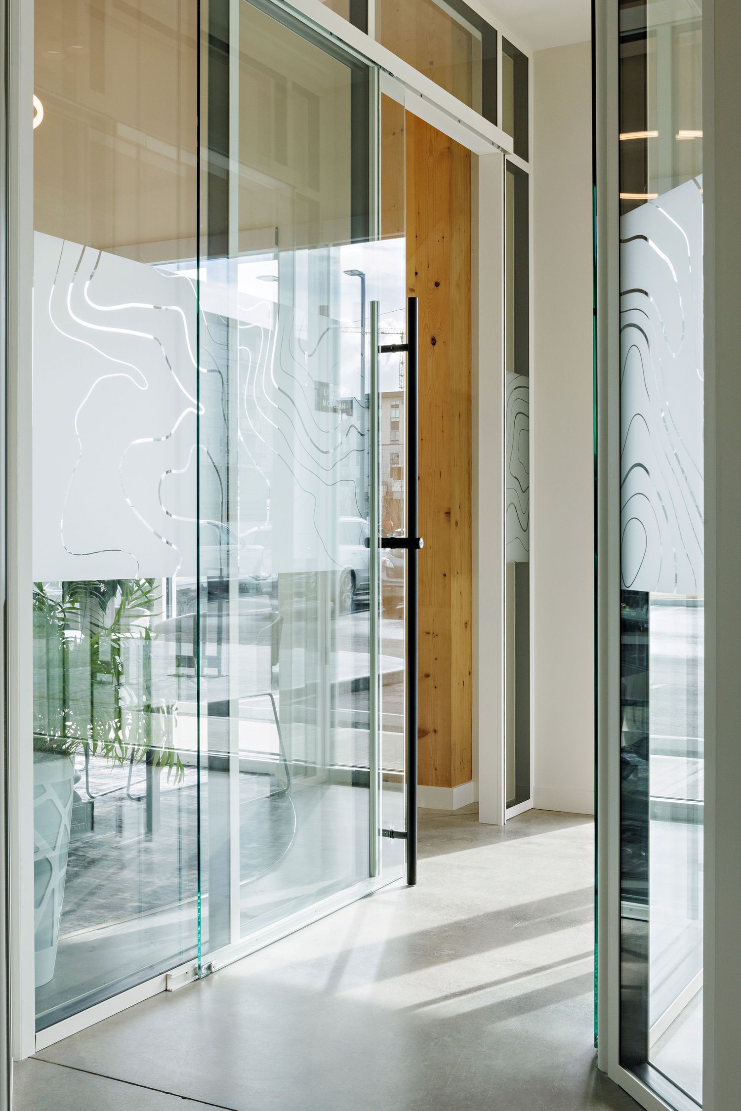 Modern office interior with glass walls featuring frosted wave patterns and light wood accents in a bright minimalist design.