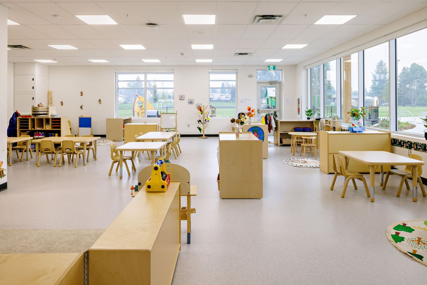 Modern educational classroom with natural lighting features light wood furniture, white walls, and an open floor plan layout.