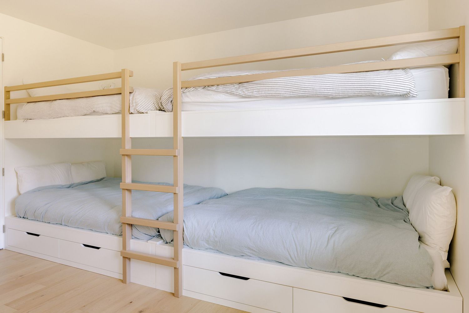 Modern white bunk beds with built-in storage drawers underneath feature pale blue bedding in a minimalist bedroom design.