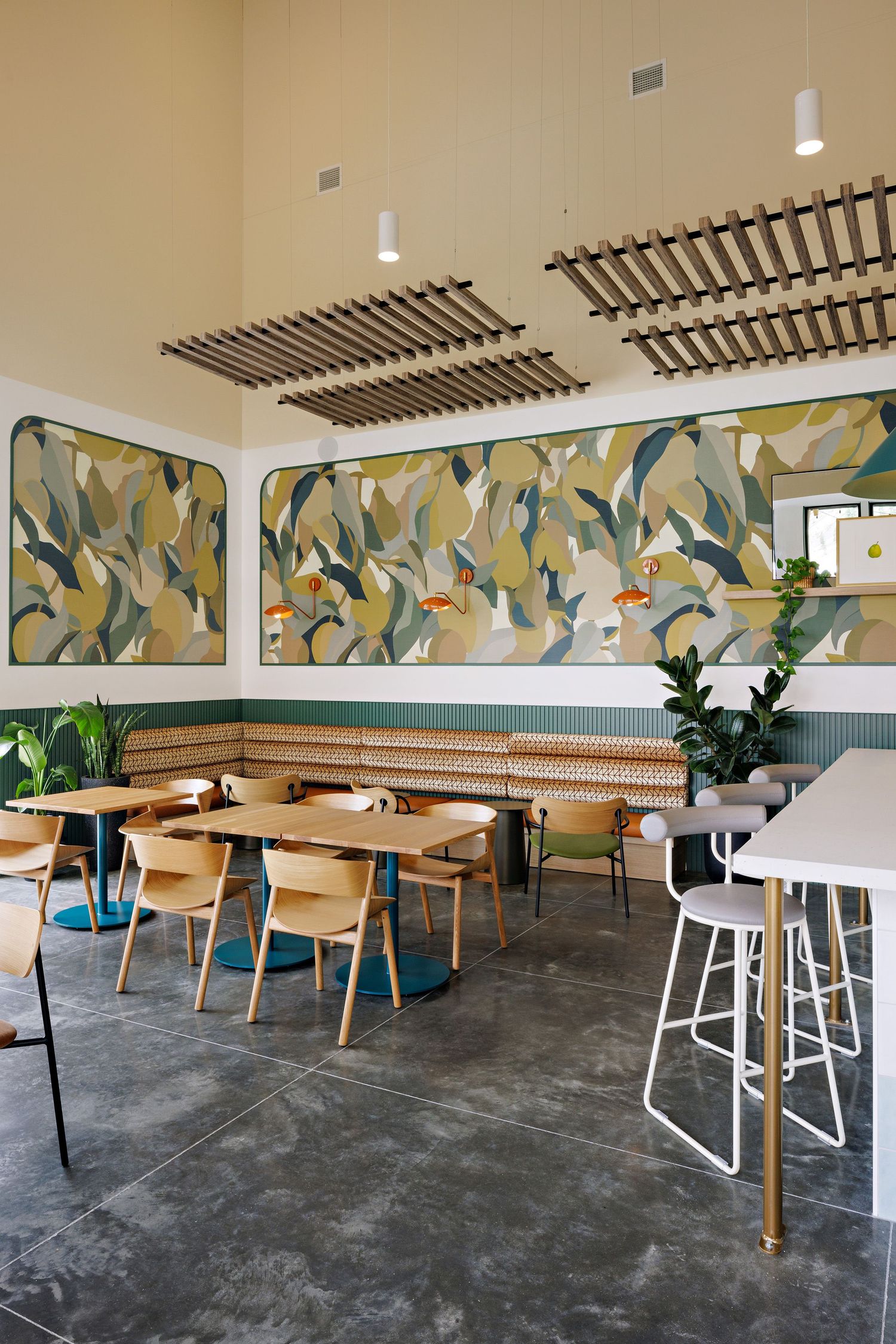 Modern cafe interior with wooden furniture, decorative wall mural in green and yellow tones, and trendy trellis ceiling details.
