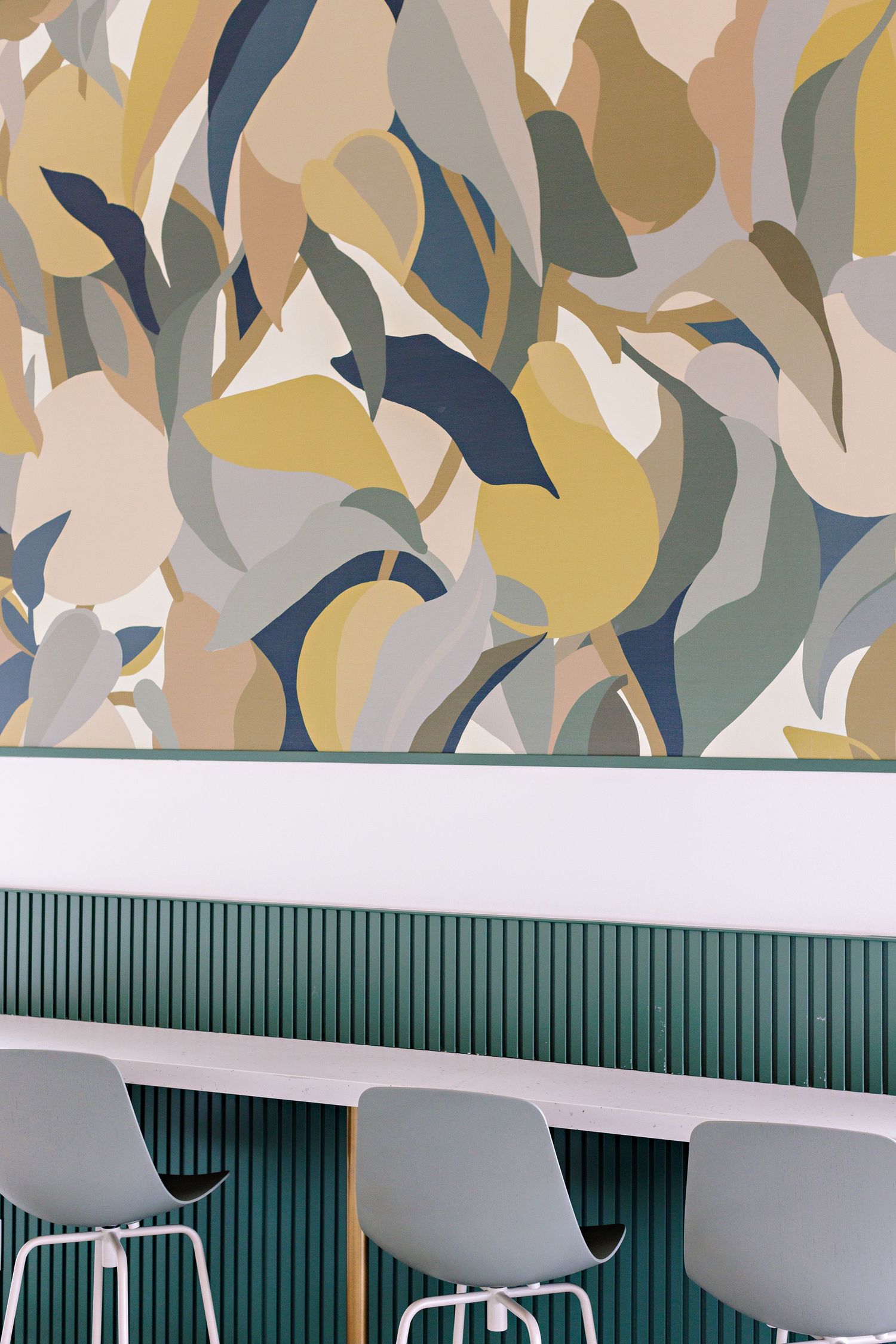 Modern interior design with abstract floral wallpaper in muted tones above green paneling and gray bar stools.