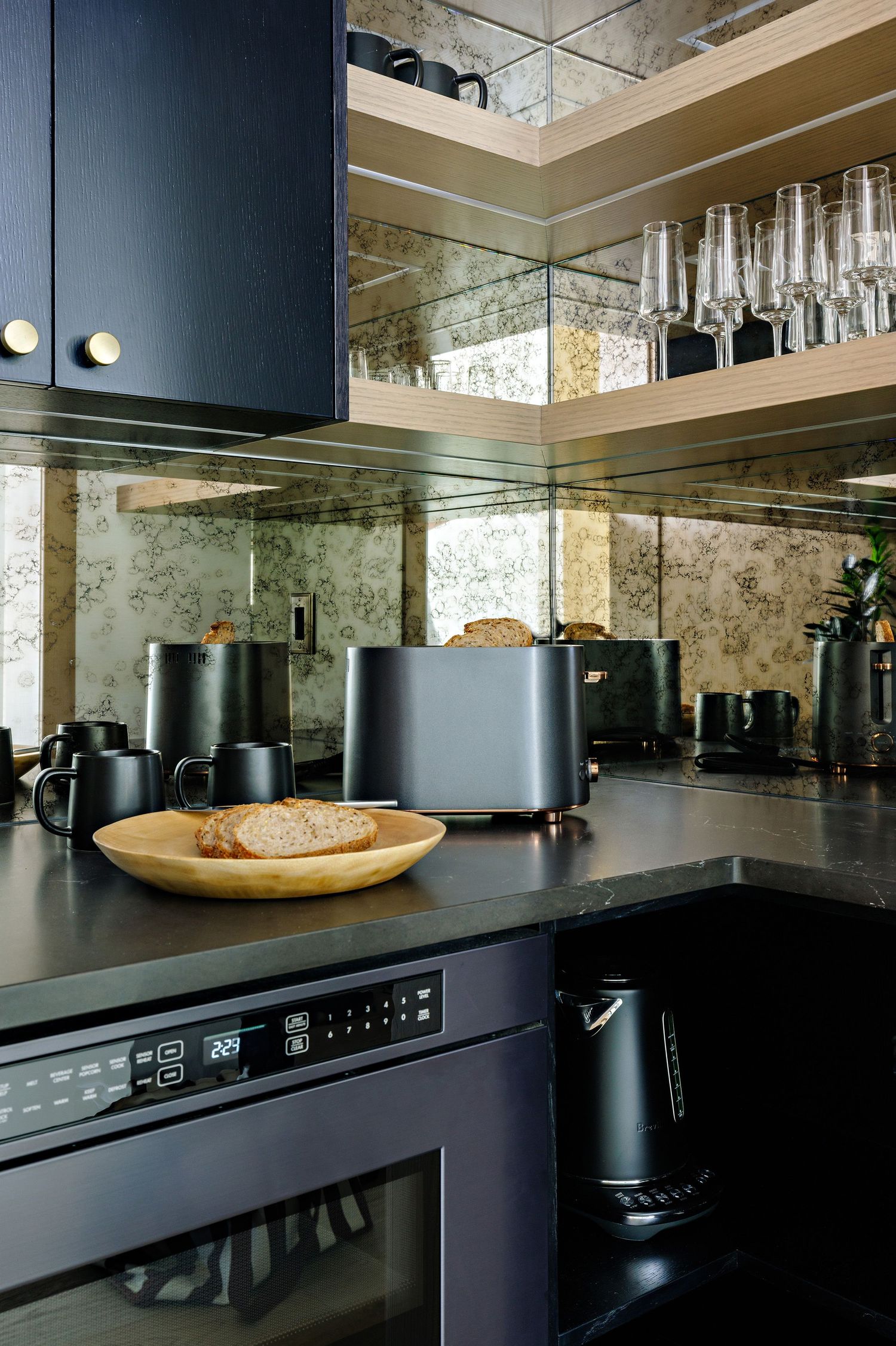 Kitchen counter with black appliances, toaster, and glassware displayed on mirrored backsplash.