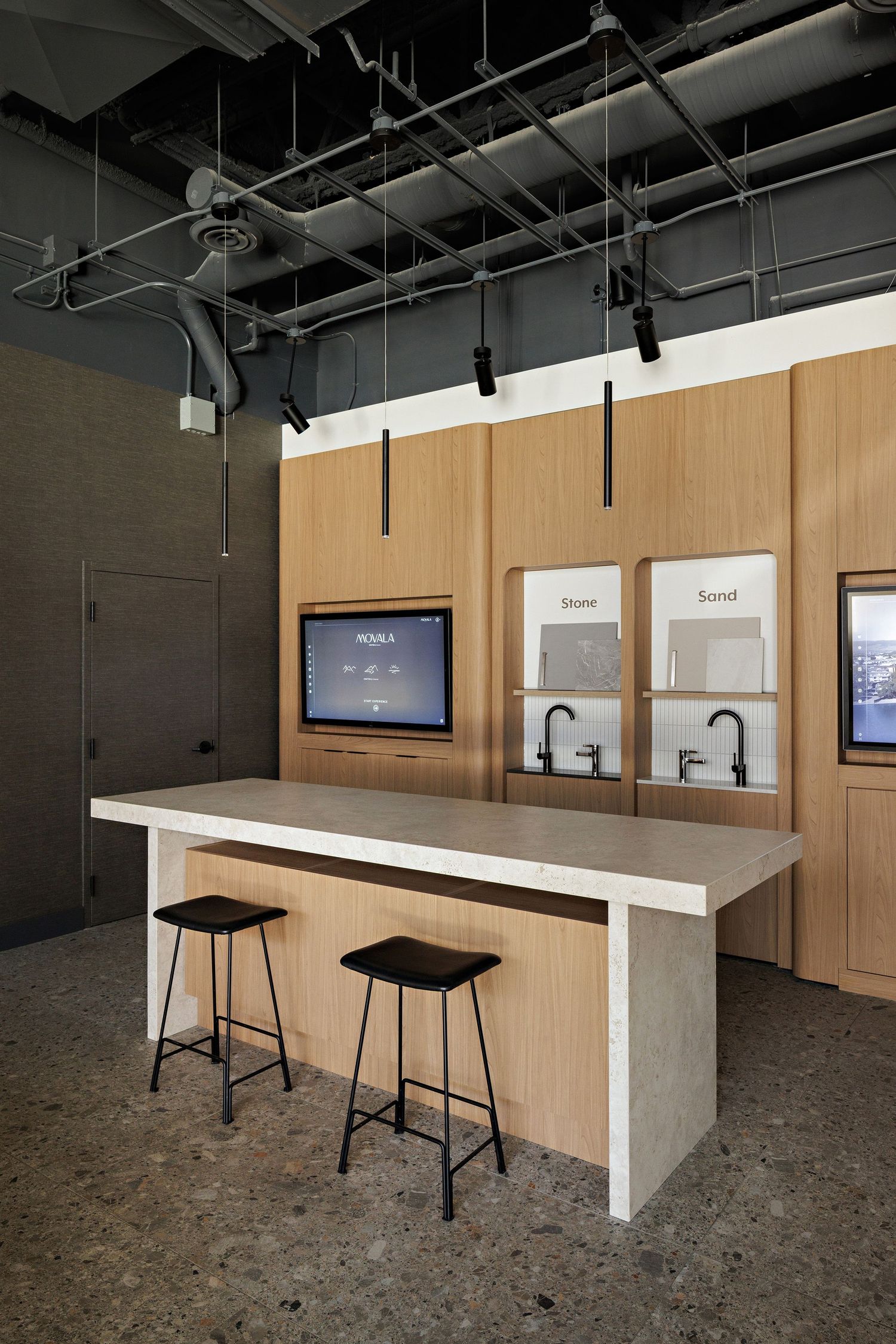 Modern industrial showroom featuring a white counter with black stools and wood paneled wall displays with embedded screens.