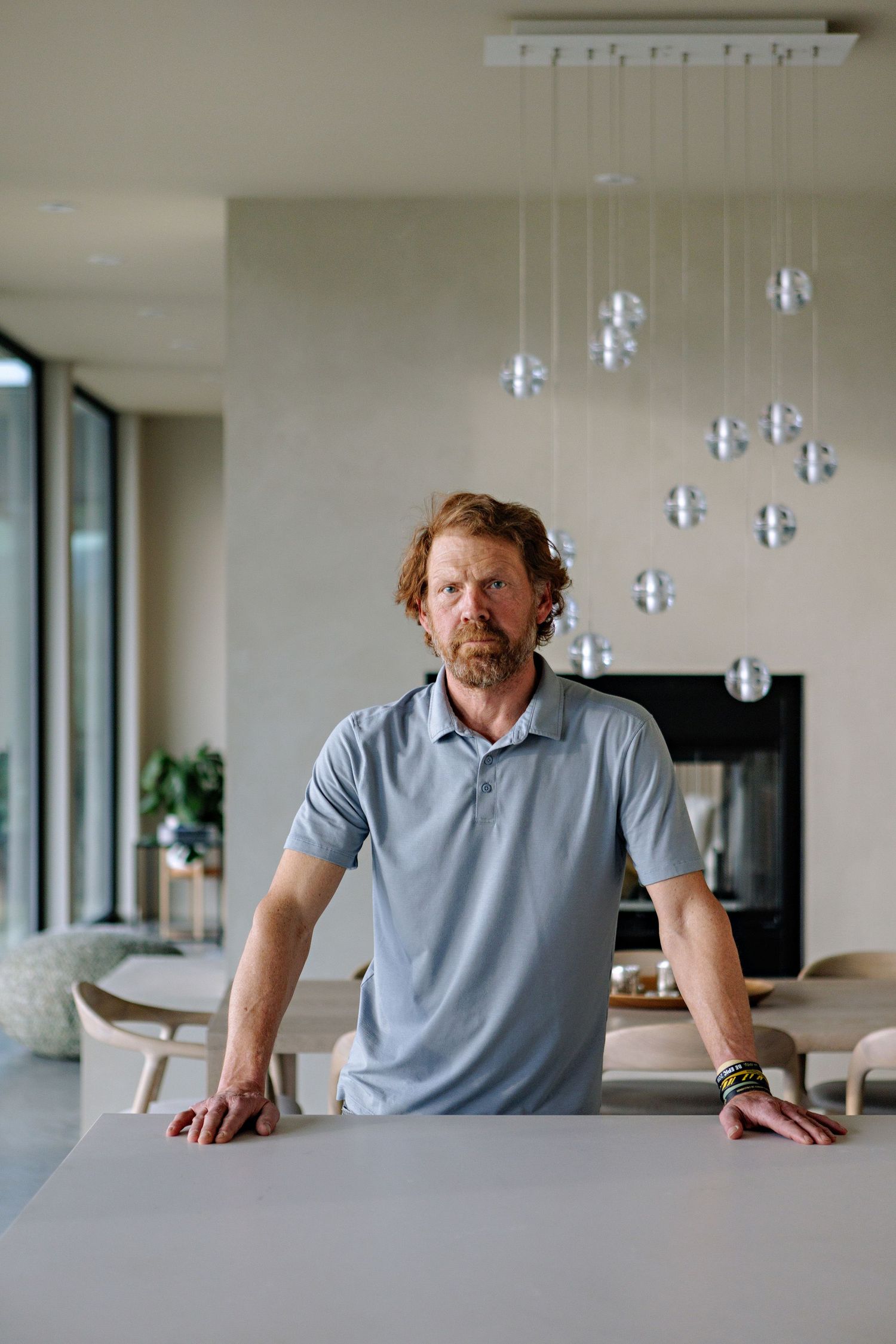 Person standing at a modern white table under glass pendant lights in a minimalist dining space.