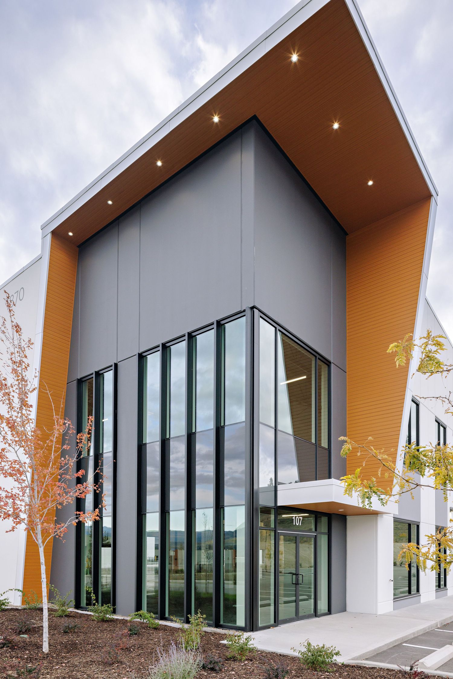 Modern commercial building exterior with angular gray and orange facade featuring floor-to-ceiling windows.