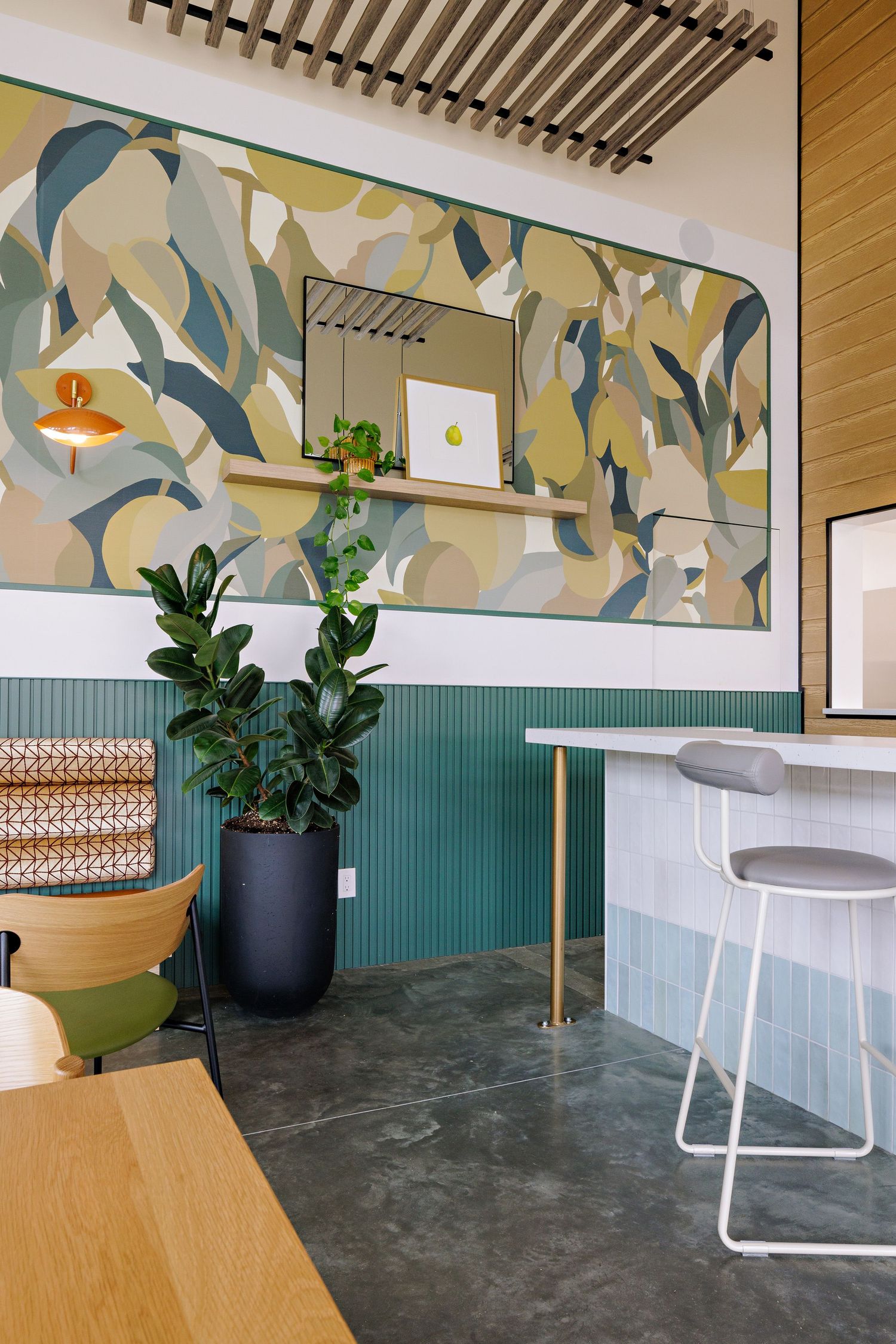 Modern restaurant interior with abstract mural, teal wainscoting, potted plants, and minimalist white bar stools.