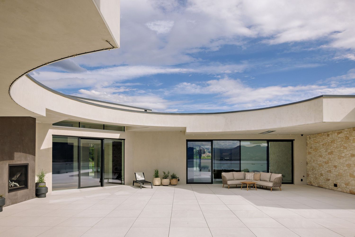 Modern curved patio with glass walls and stone accents showcases contemporary architecture under blue skies.