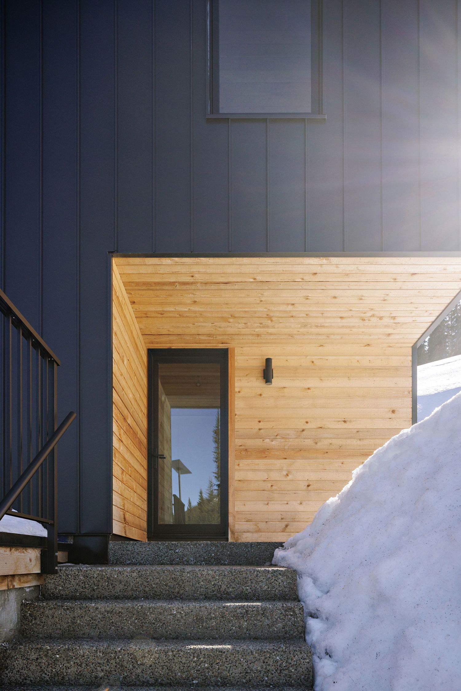 Modern entryway with wooden accent wall and concrete steps covered in snow.