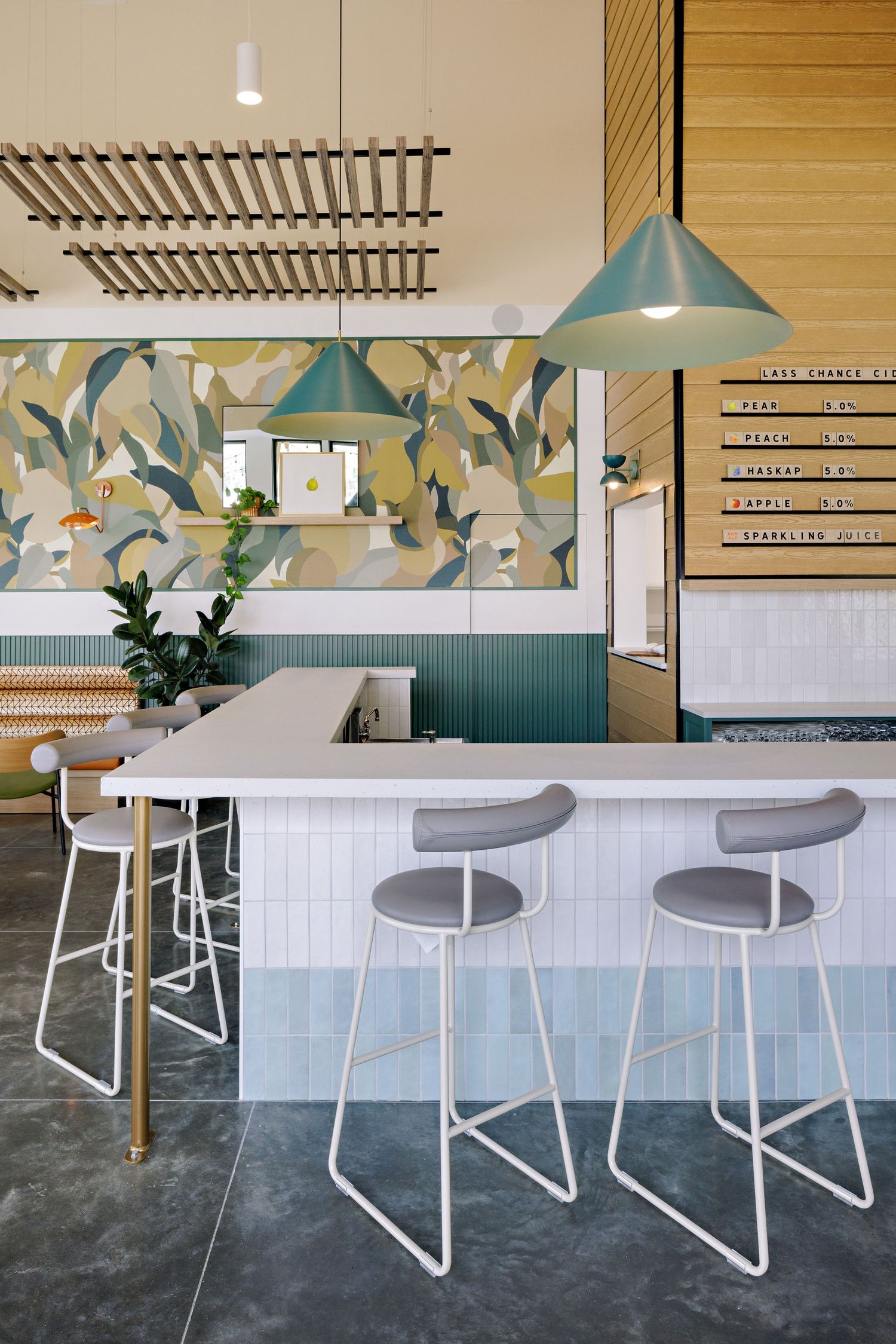 Modern restaurant interior with teal pendant lights, white bar counter, and geometric wall mural in muted green tones.