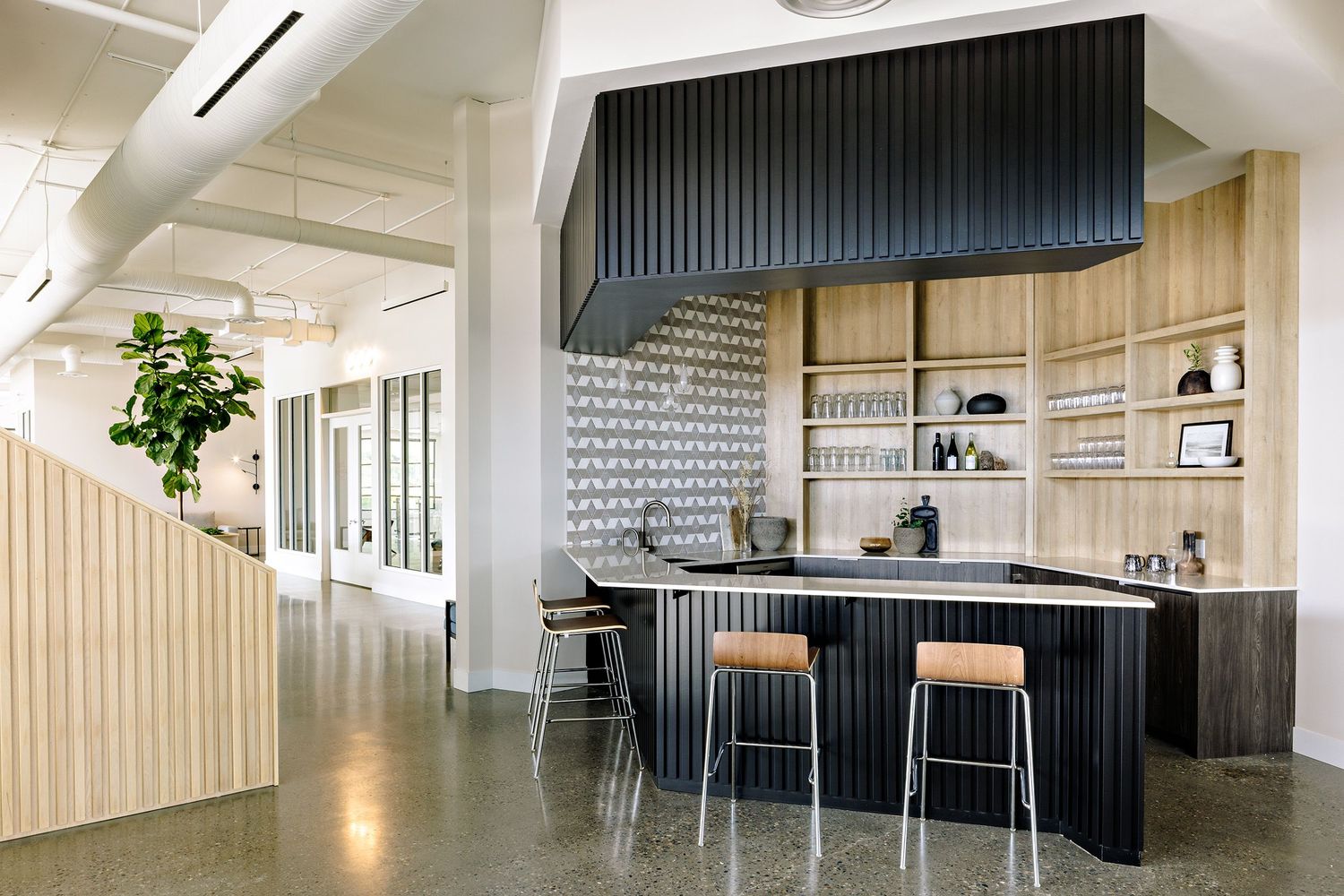Modern office break room with sleek black bar counter, wooden wall panels, and industrial concrete floors in minimalist design.