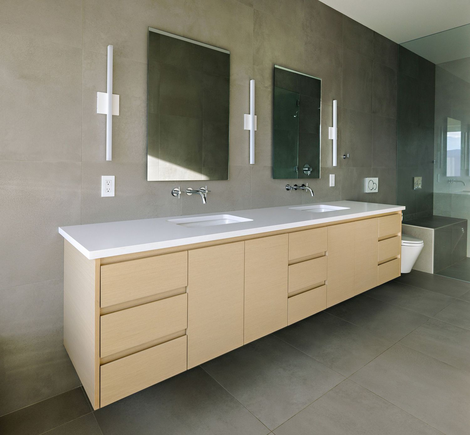 Modern floating bathroom vanity with cream-colored drawers, white countertop, and sleek wall sconces against gray walls.