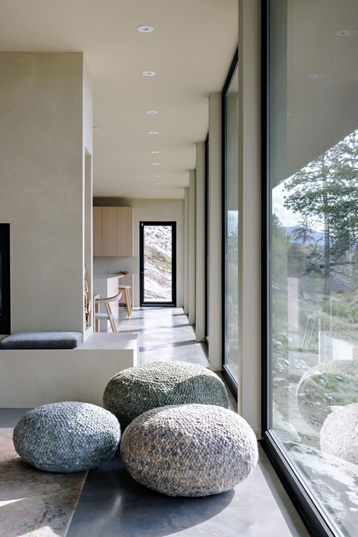 Modern hallway with floor-to-ceiling windows and knitted pouf ottomans overlooking scenic mountain views.