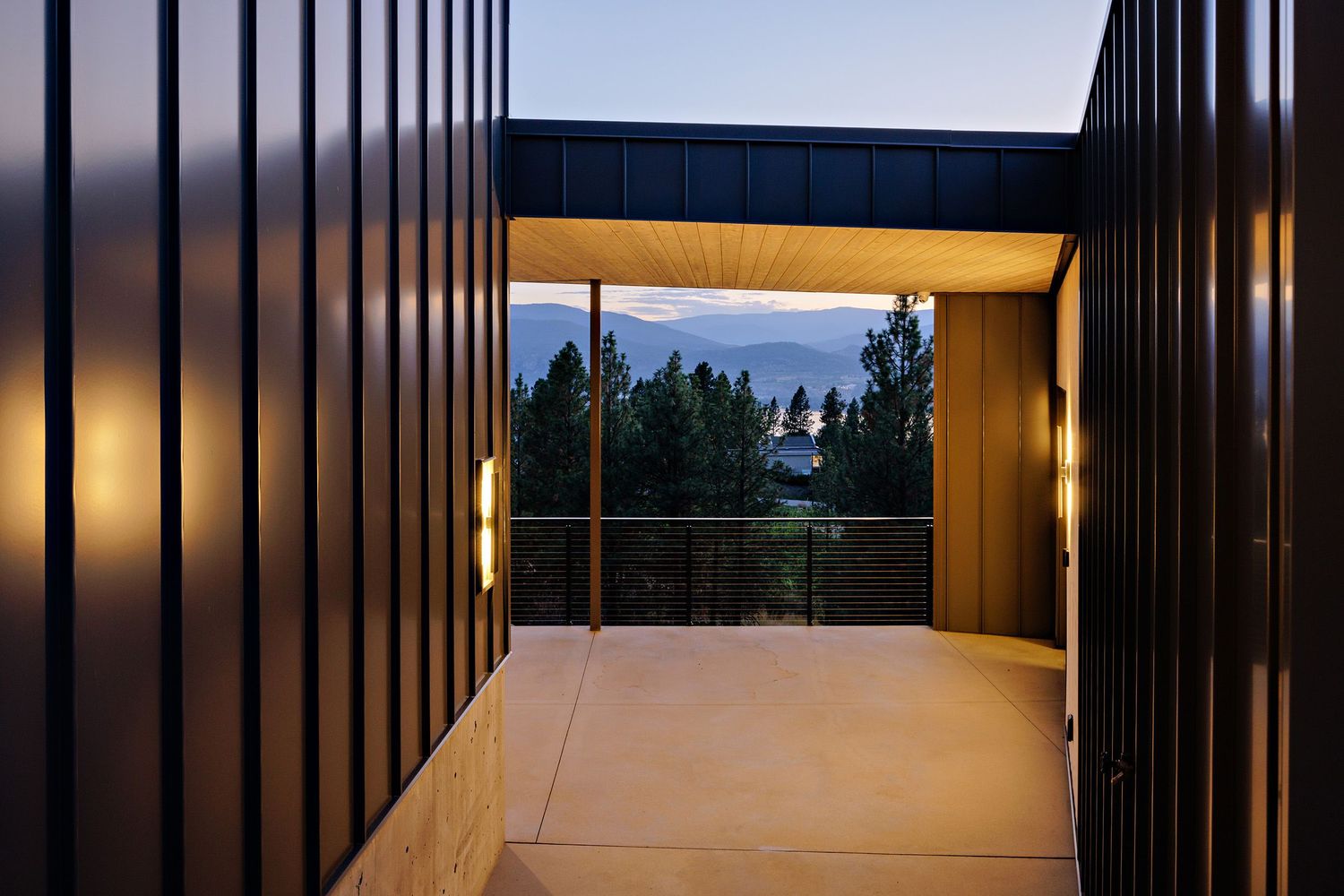 Modern architectural corridor with vertical metal slats framing a scenic twilight view through glass windows at the end.