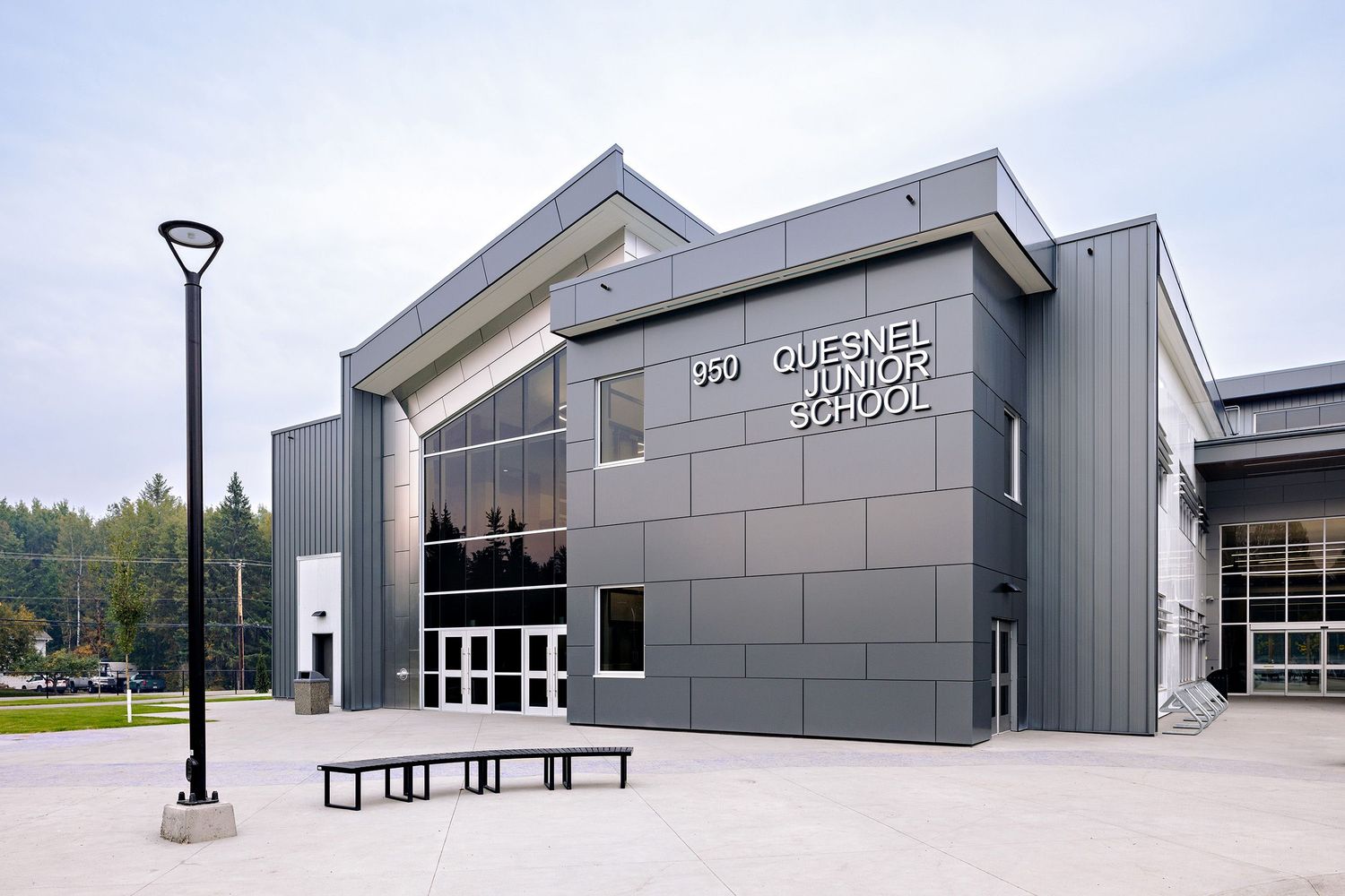 Modern gray school building exterior with glass entrance doors and contemporary architectural design under cloudy sky.