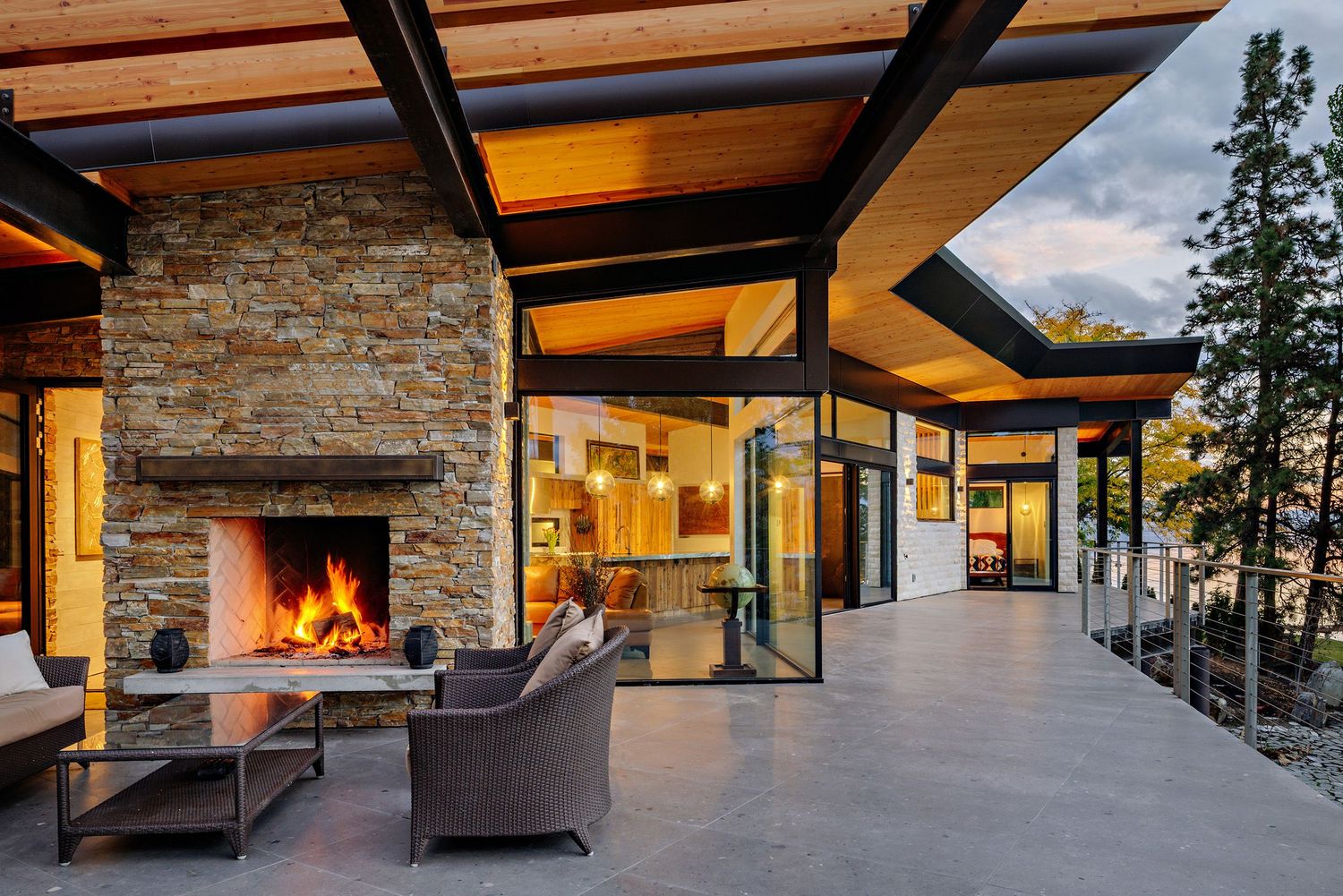 Modern luxury mountain home with stone exterior features expansive windows and outdoor living spaces at sunset.