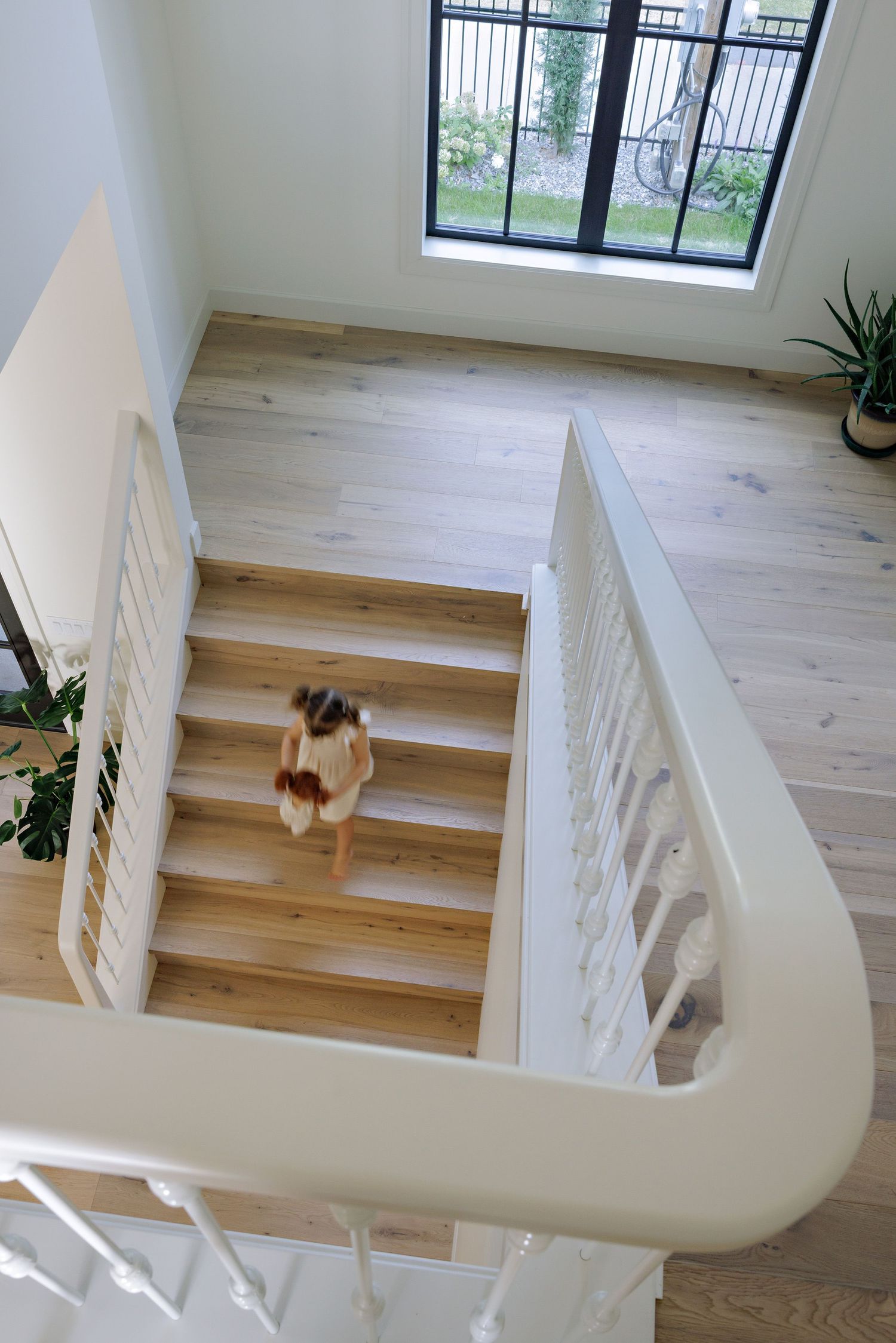 Modern wooden staircase with white railings and natural light streaming through a window in a minimalist interior.