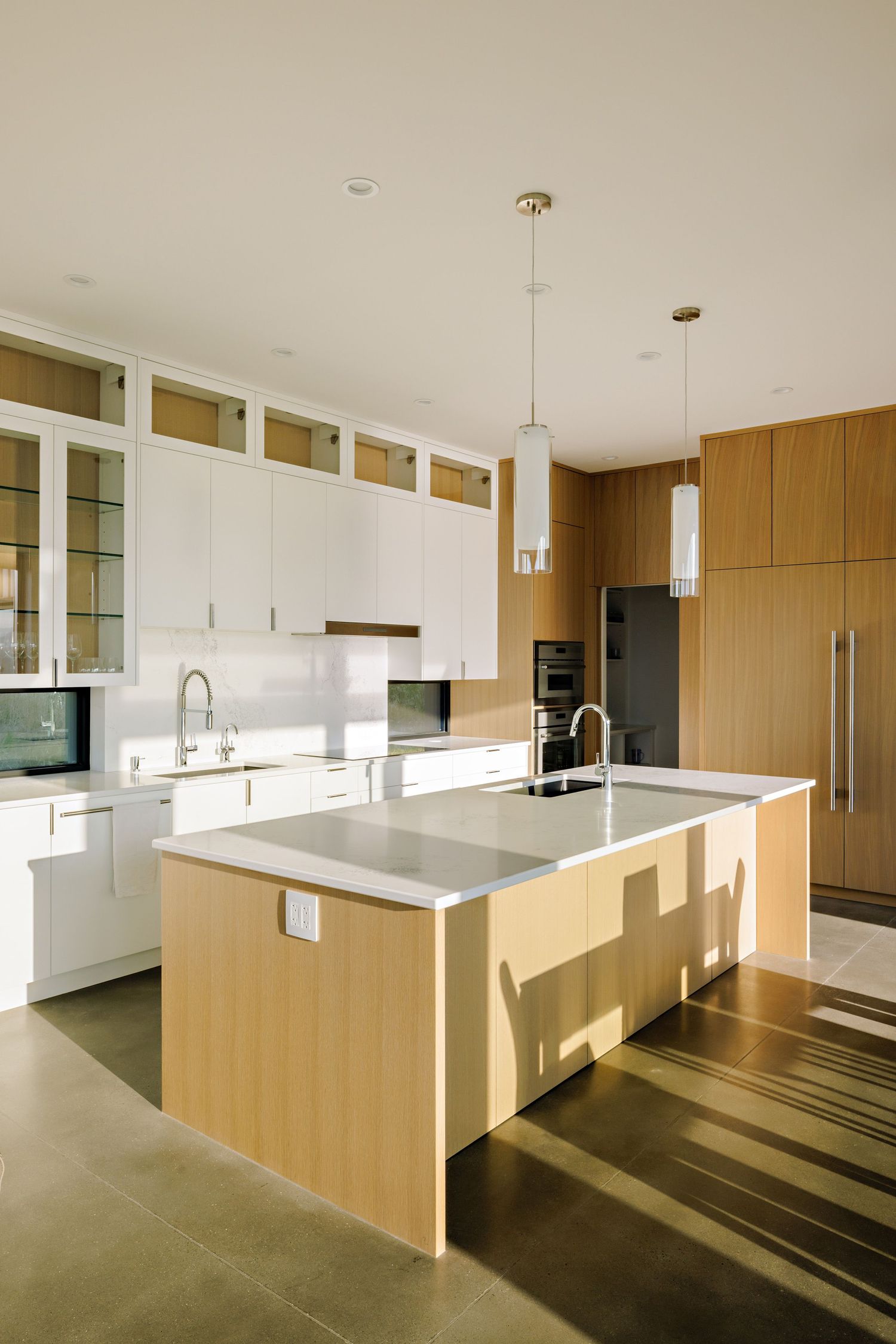 Modern kitchen with white cabinetry and light wood island featuring pendant lights and stainless steel appliances.