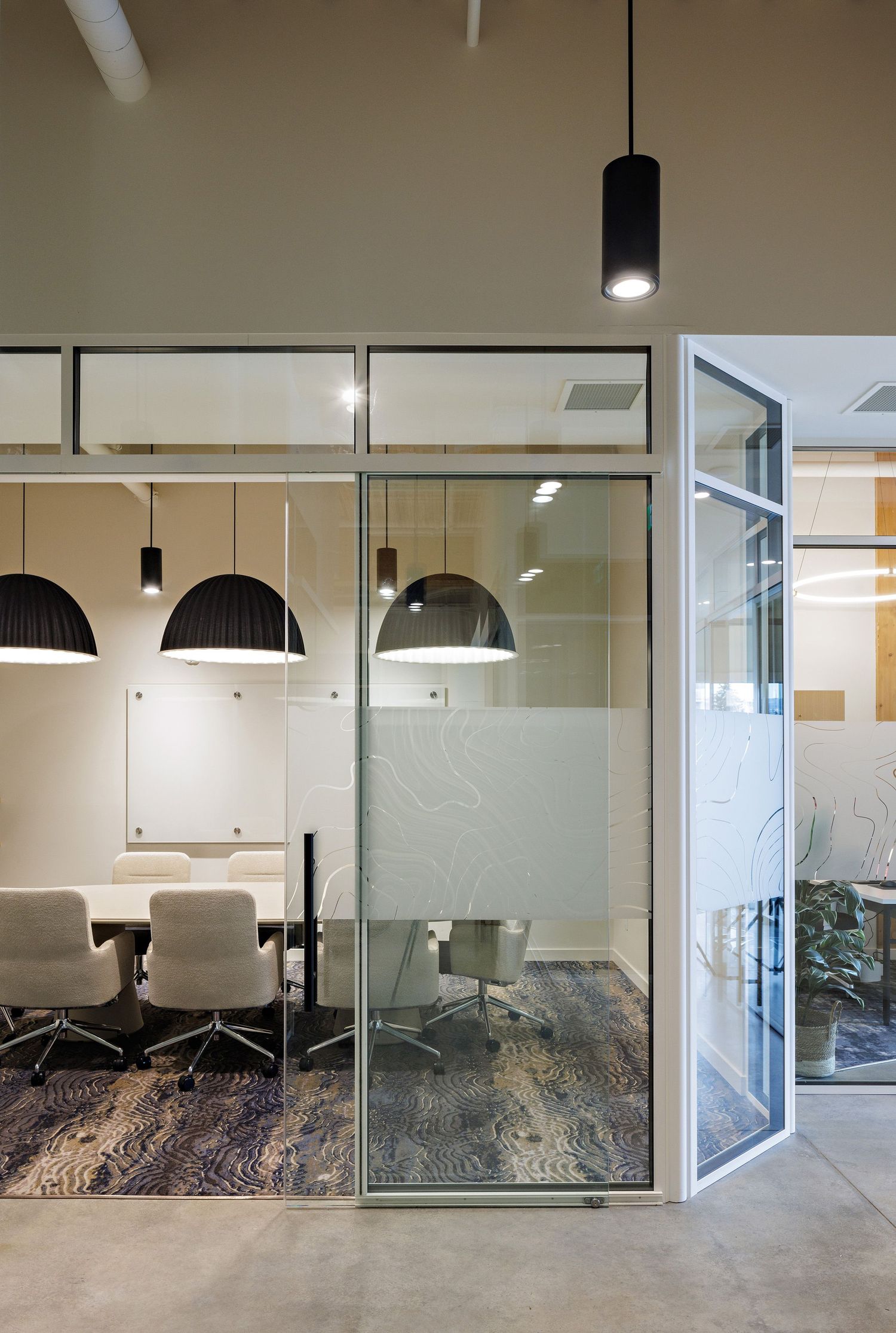 Modern office meeting room with glass walls, pendant lights, and frosted privacy panels in a contemporary workspace design.