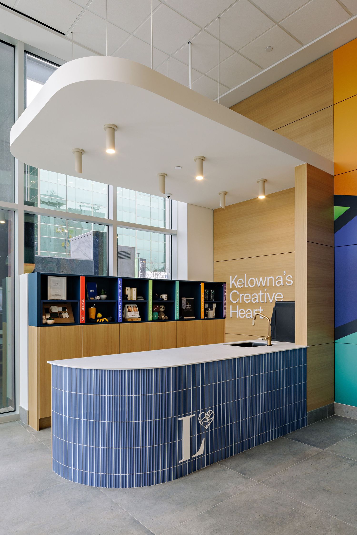 Modern reception desk with curved blue tile front and white countertop under floating ceiling panel in bright office space.