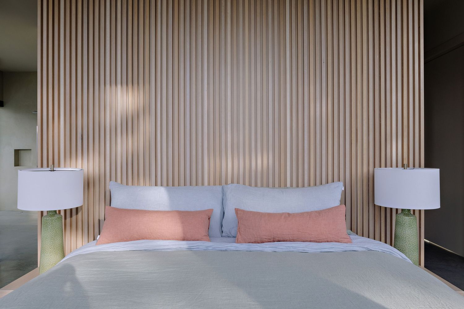 Modern bedroom interior with vertical wood slat wall, white bedding, coral pillows and matching table lamps.