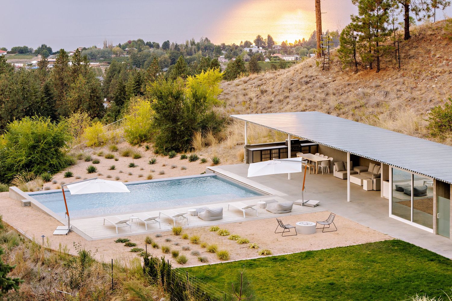 Modern hillside home with infinity pool, covered patio and landscaped yard surrounded by mountain views at sunset.